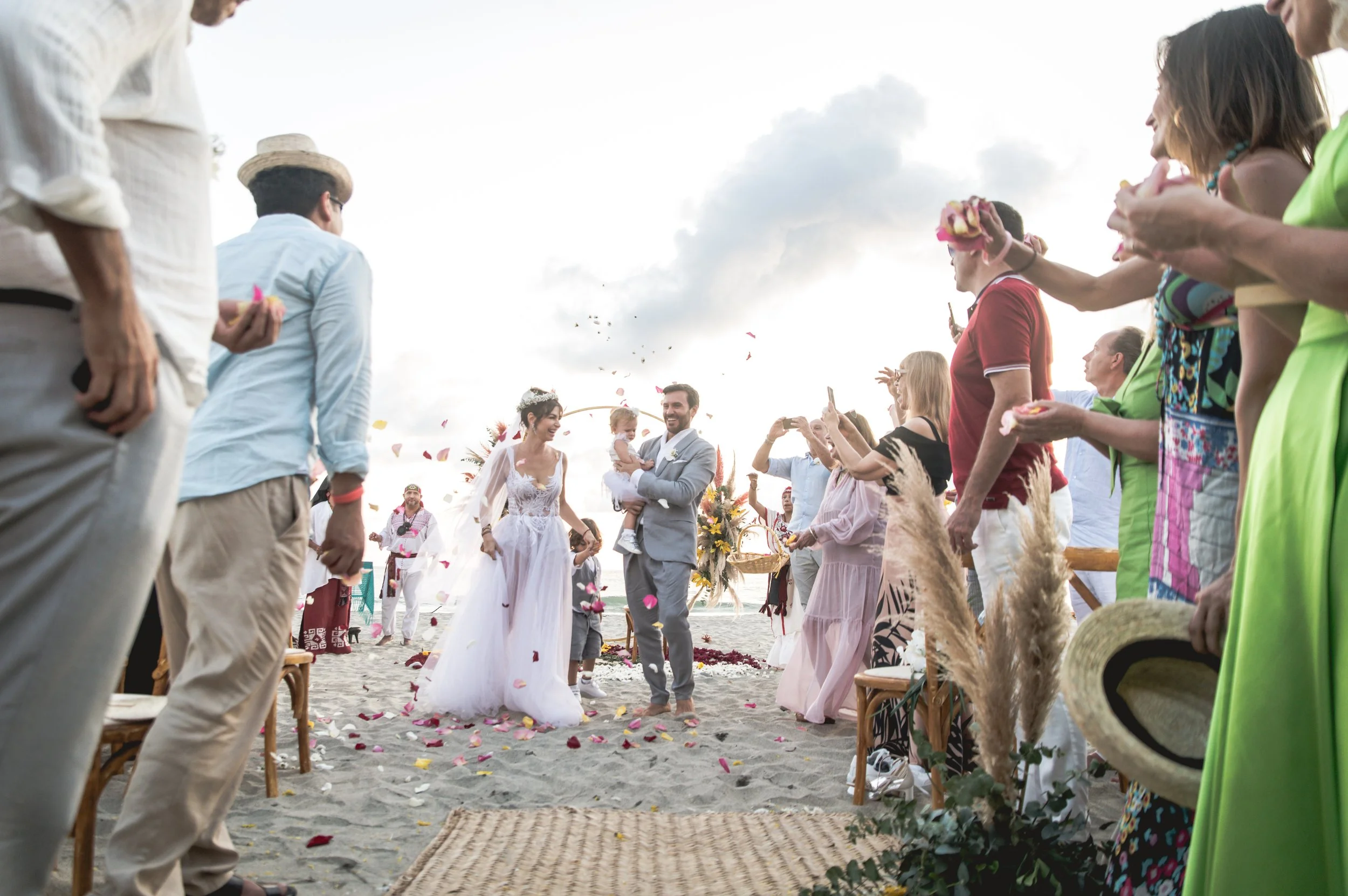 Wedding ceremony in Puerto Escondido where a couple from Europe are walking the alley and people throwing petals in front a beautiful sunset at the beach in Puerto Escondido. Amazing frame and luxurious wedding.