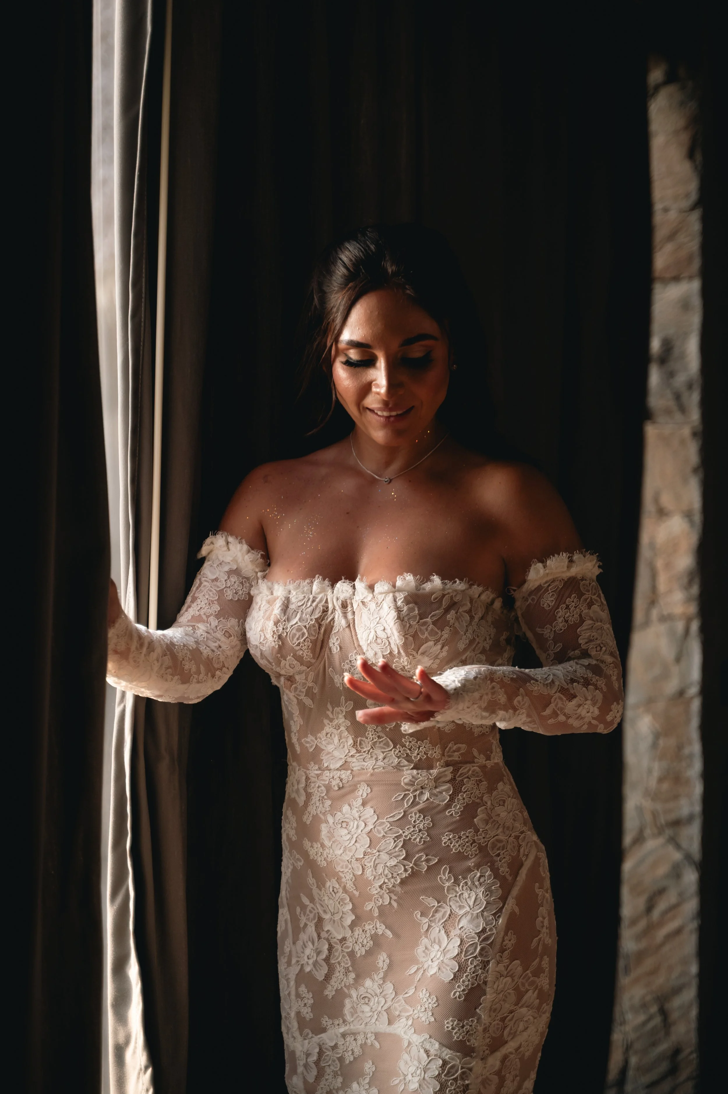 Beautiful profesional wedding photography of a bride looking at her engagement ring in front of a window with her beautiful wedding dress in a luxury villa in Puerto Escondido.