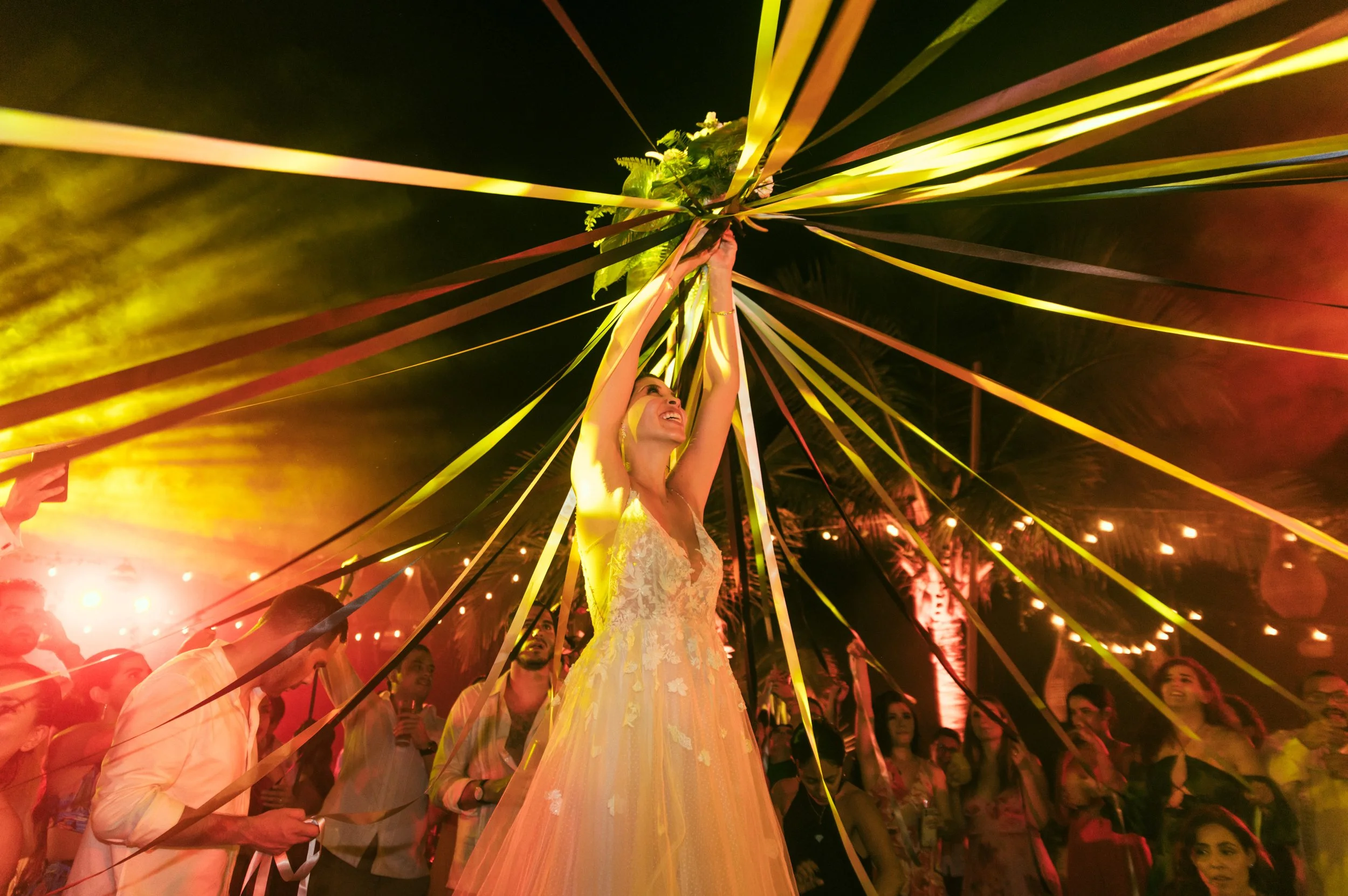 Bride holding her floral composition in har wedding party with all her guest around her. colorfull image of a party in Puerto Escondido 