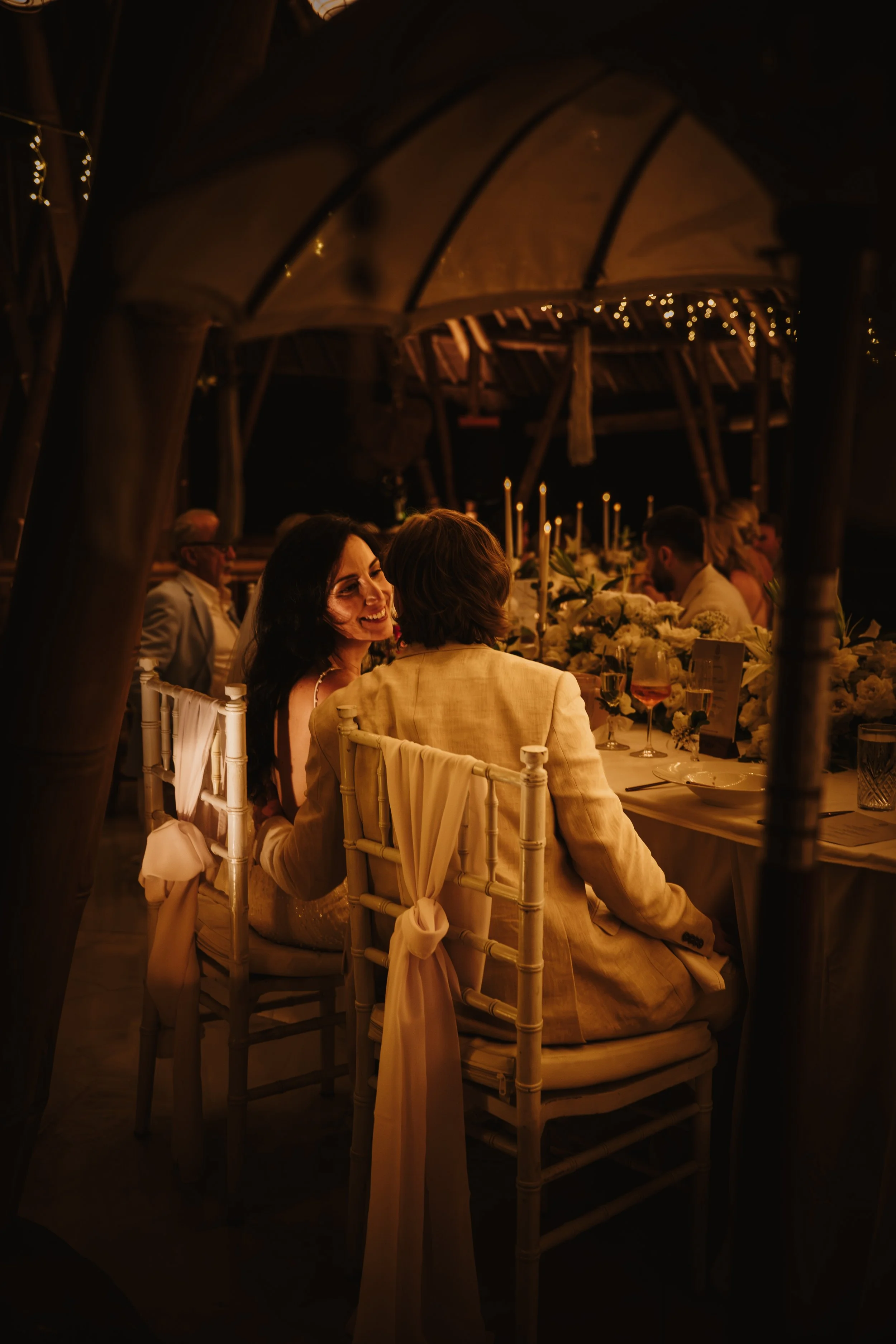 Bali villa wedding dinner — bride and groom sharing tender, loving glances across the table during an intimate candlelit dinner at Kanyon Ubud jungle resort.