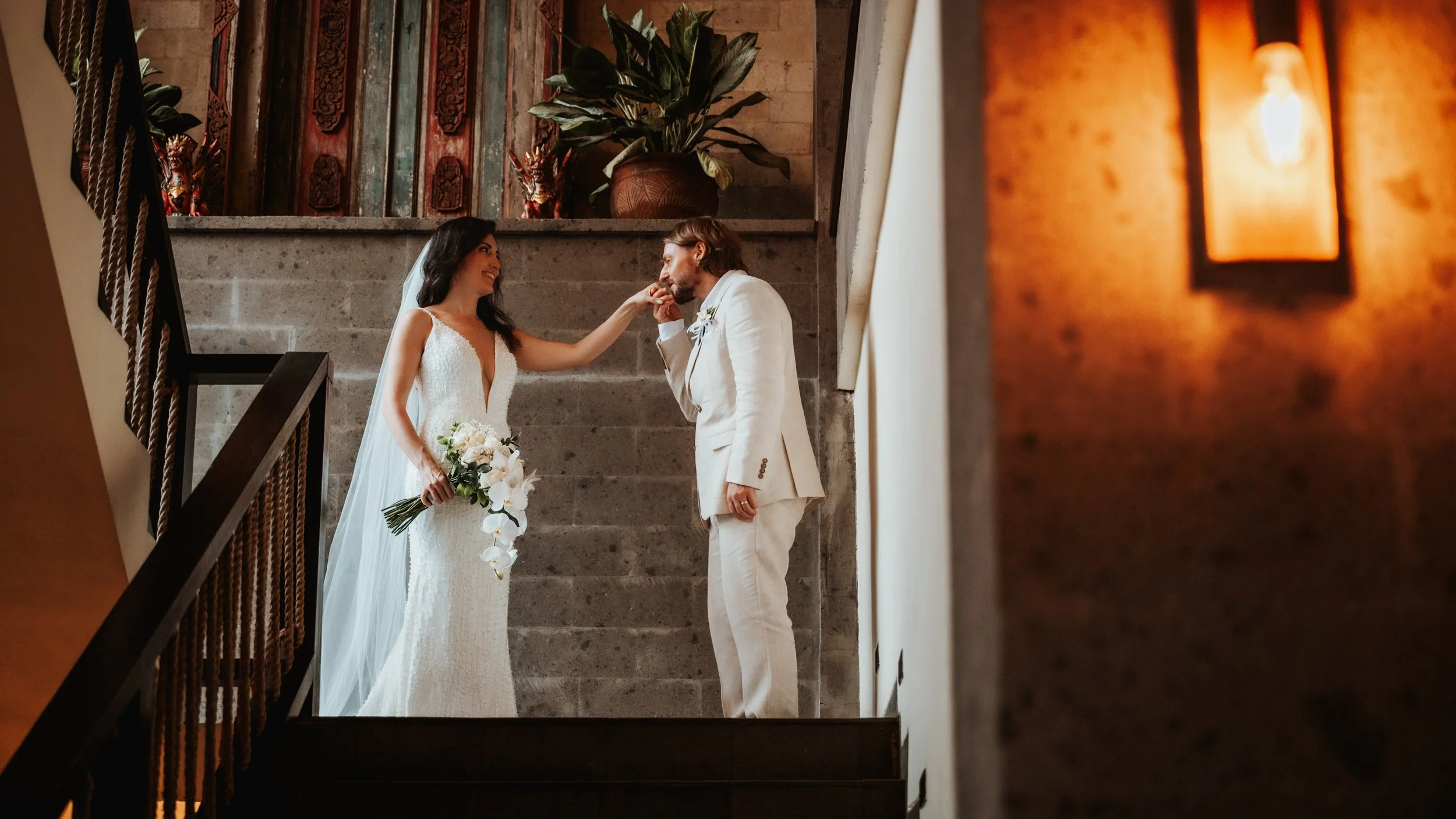 Bali jungle wedding staircase — bride and groom running hand-in-hand down a stone staircase framed by dense rainforest, Kanyon Ubud villa resort.