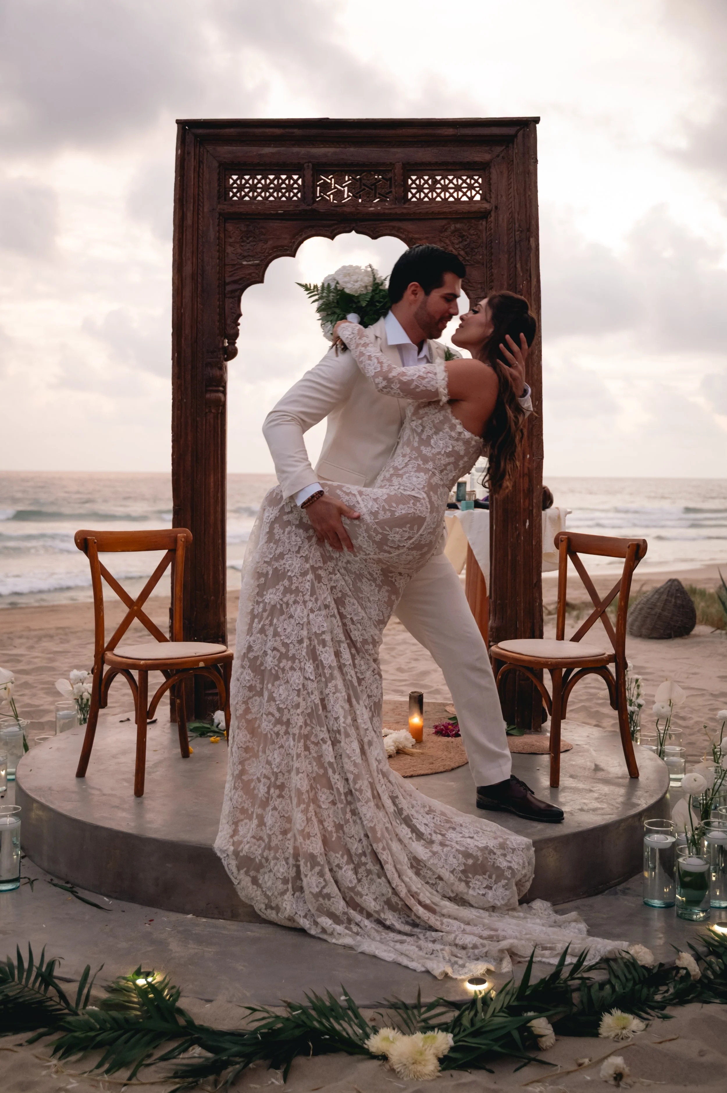 End of the ceremony of a wedding in Puerto Escondido where a Mexican couple from Cancun are embracing and kissing in front a beautiful sunset at the beach in Puerto Escondido. Amazing frame and luxurious wedding dress.