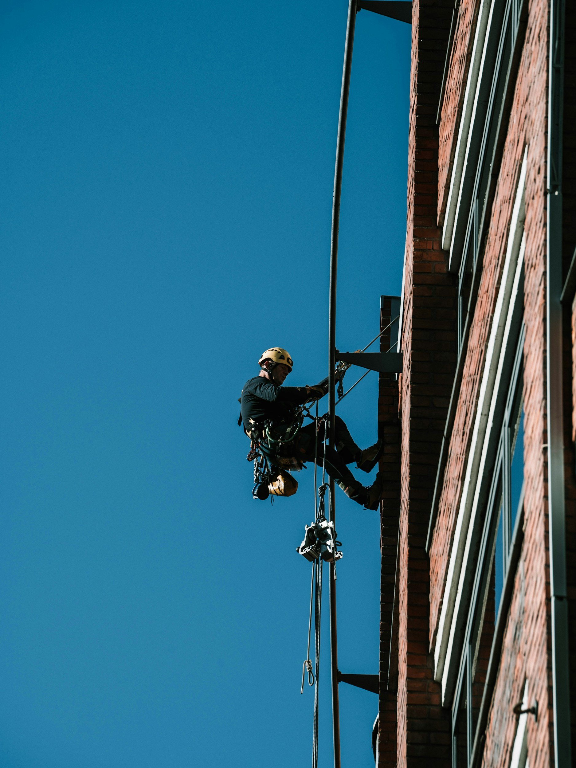 A rope access technician abseiling off the side of a red brick building.