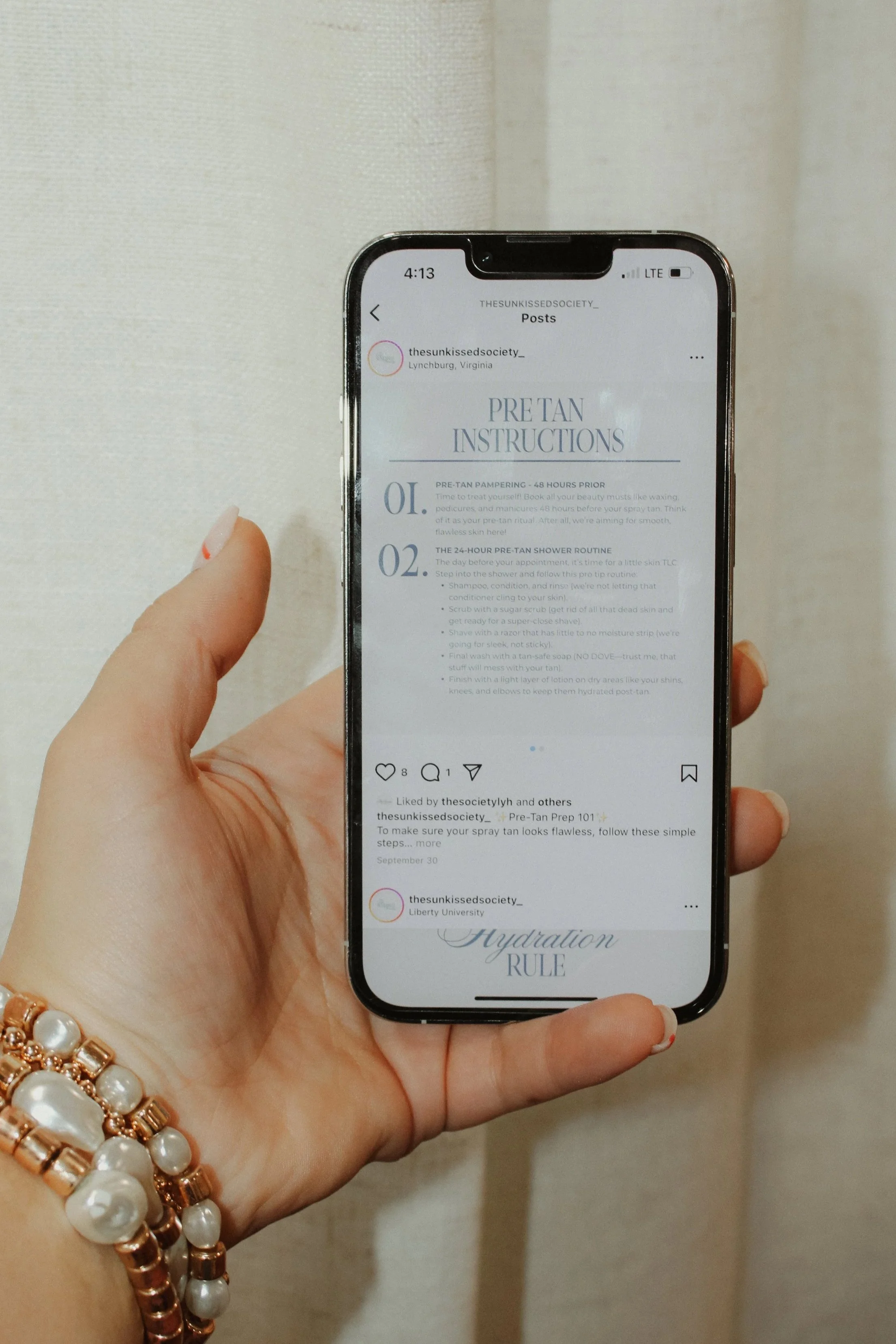 A person's hand holding a smartphone with an Instagram post open, showing a post titled 'PRE-TAN INSTRUCTIONS' from the account @thesunkissedsociety_.