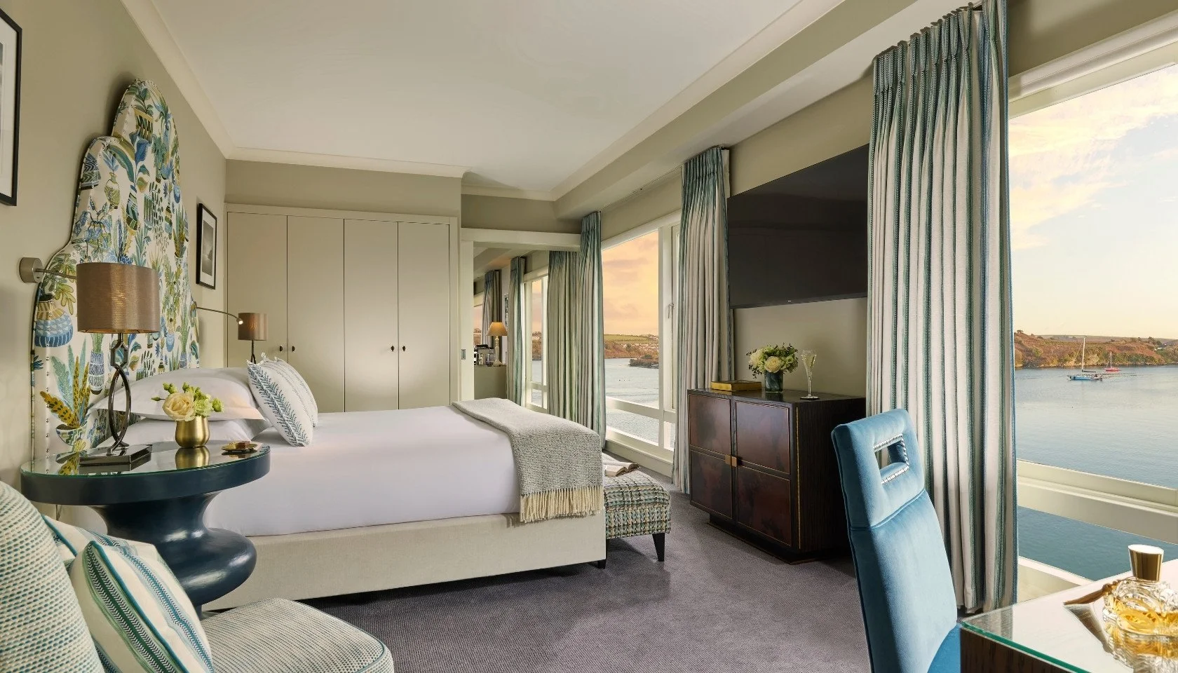 Double bed and chaise long, in front of a large screen TV, next to a floor to ceiling wardrobe.