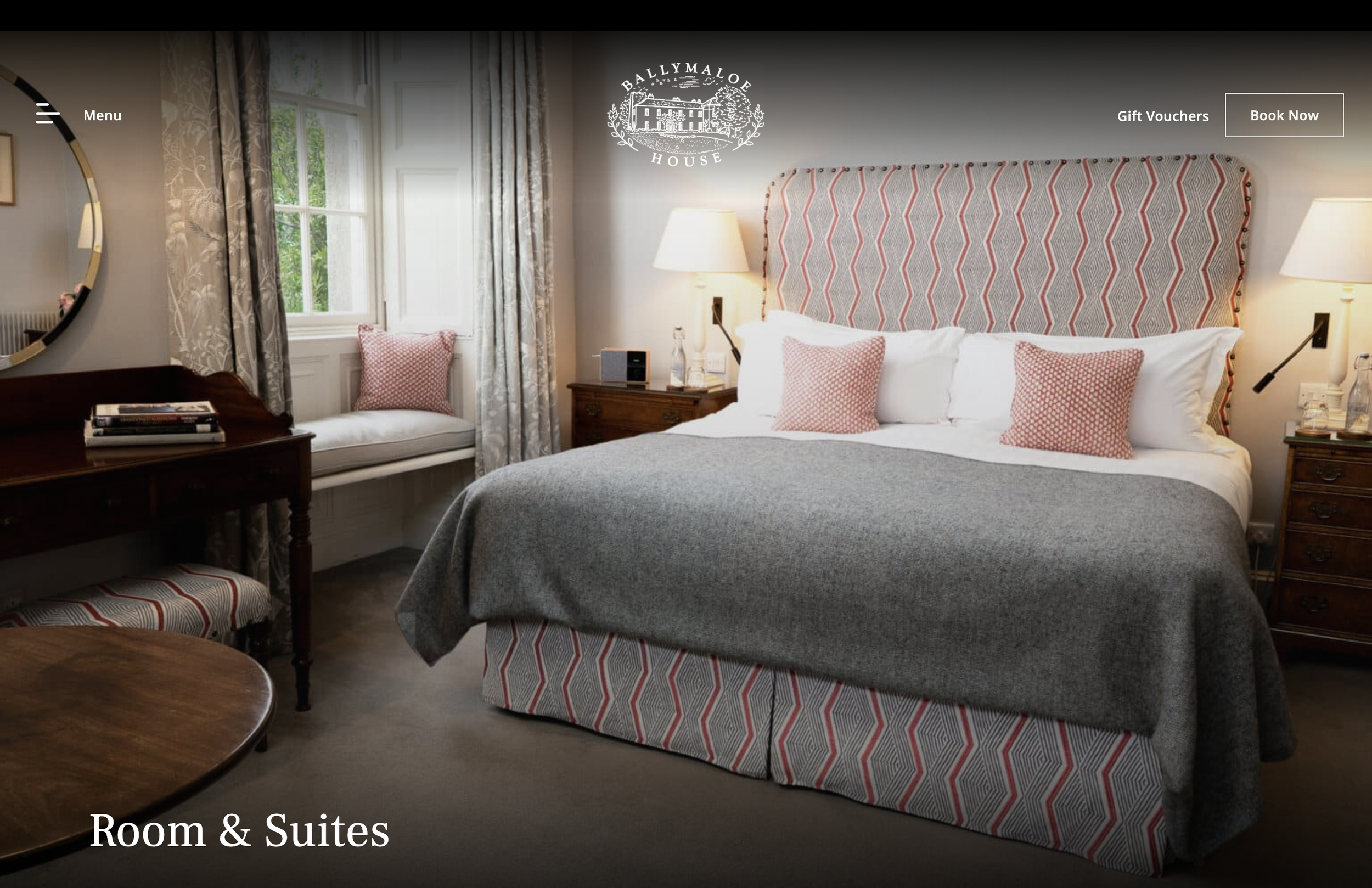 A luxurious suite featuring a king sized bed with patterned headboard and two bedside lamps.