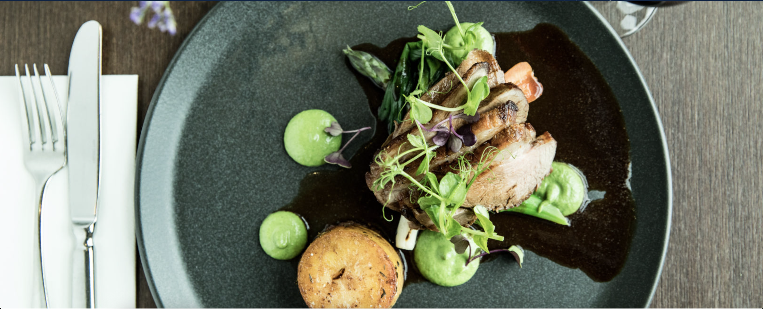 An elegantly composed overhead shot of a sliced chicken breast surrounded by pea puree and salad.