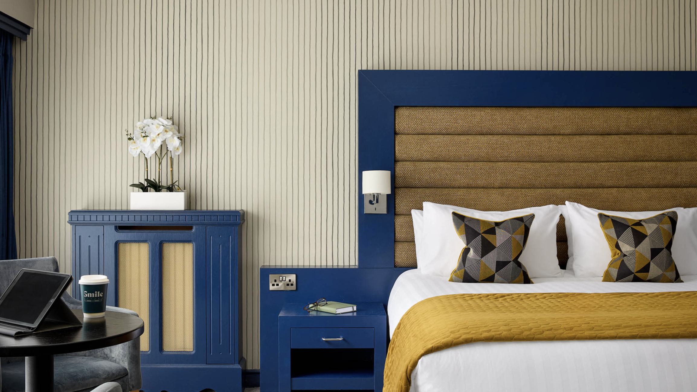 Corner of a double room with iconic blue finishes surrounding a large bed with a bright yellow throw