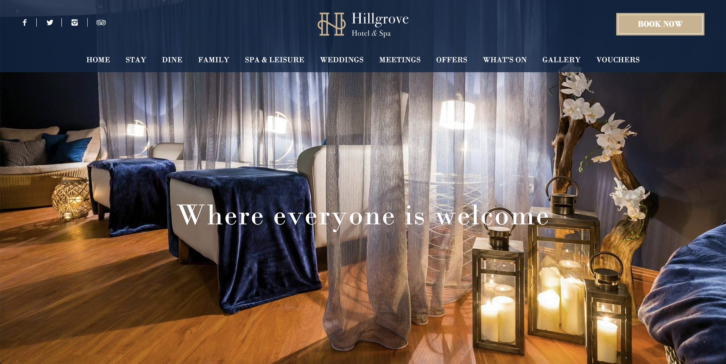 A dark, candle-lit spa room featuring two white leather beds covered in blue velvet blankets.