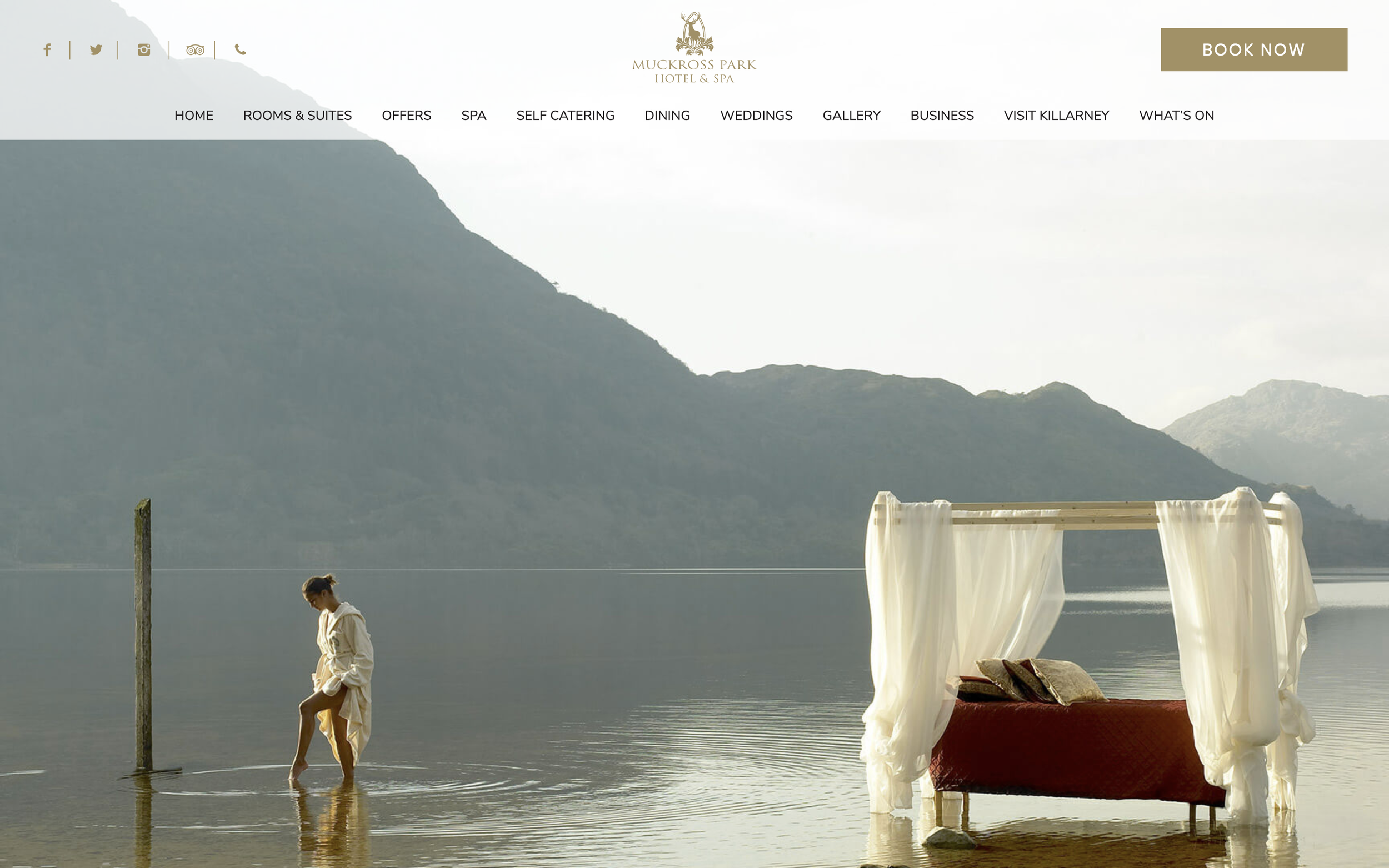 A woman in a bathrobe walking in shallow water next to a large four posters bed on the water’s edge.