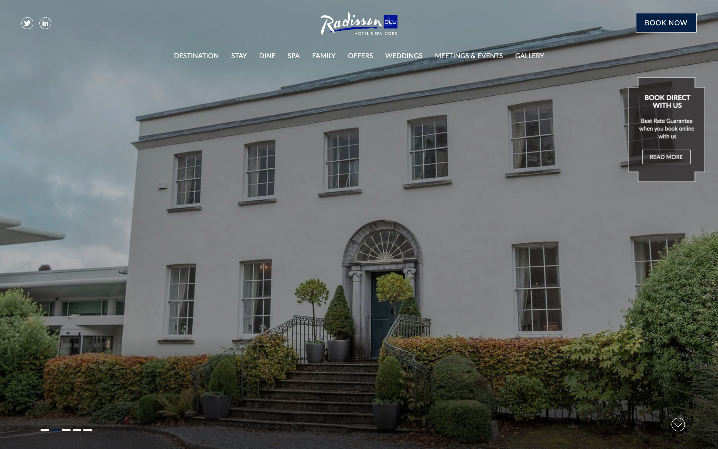 A large, white, two-story house with manicured hedges leading up to the ornate entrance door.