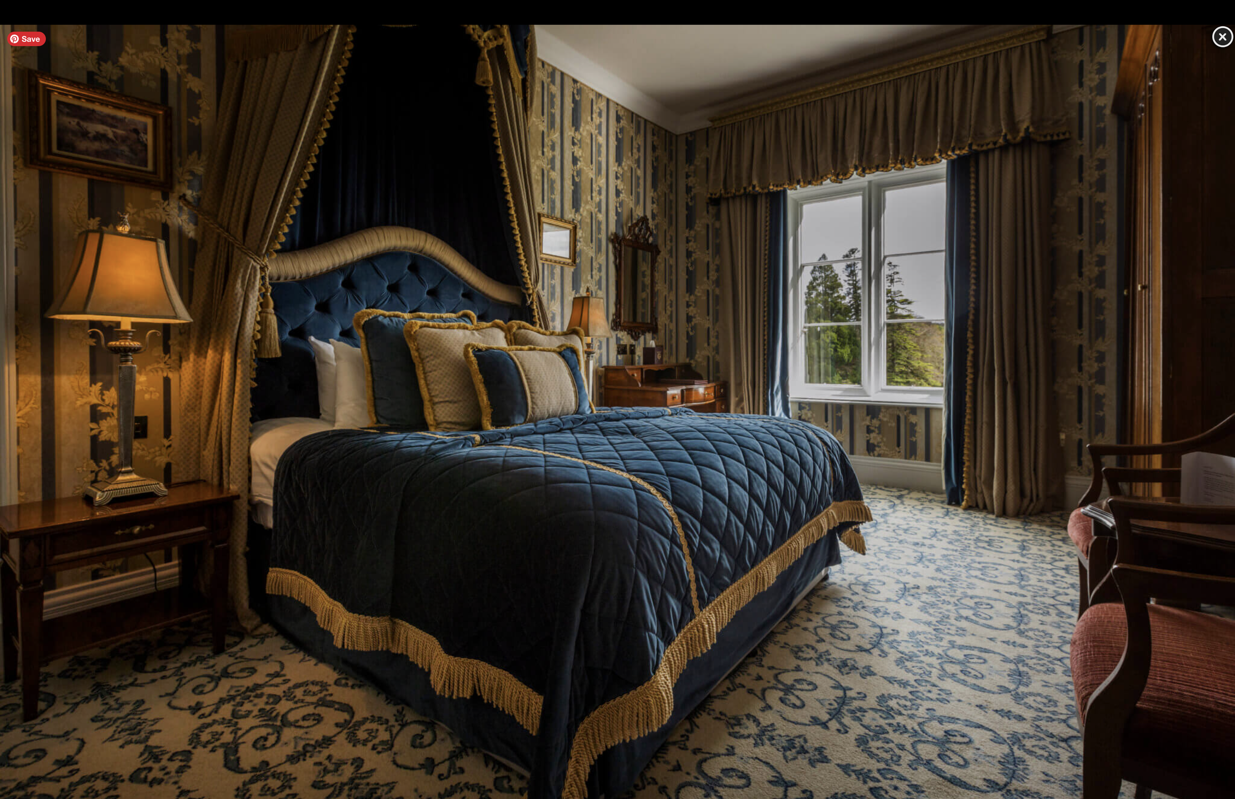 Gorgeous, gothic bedroom with large, ornate bed next to vintage lamp and large bay window.