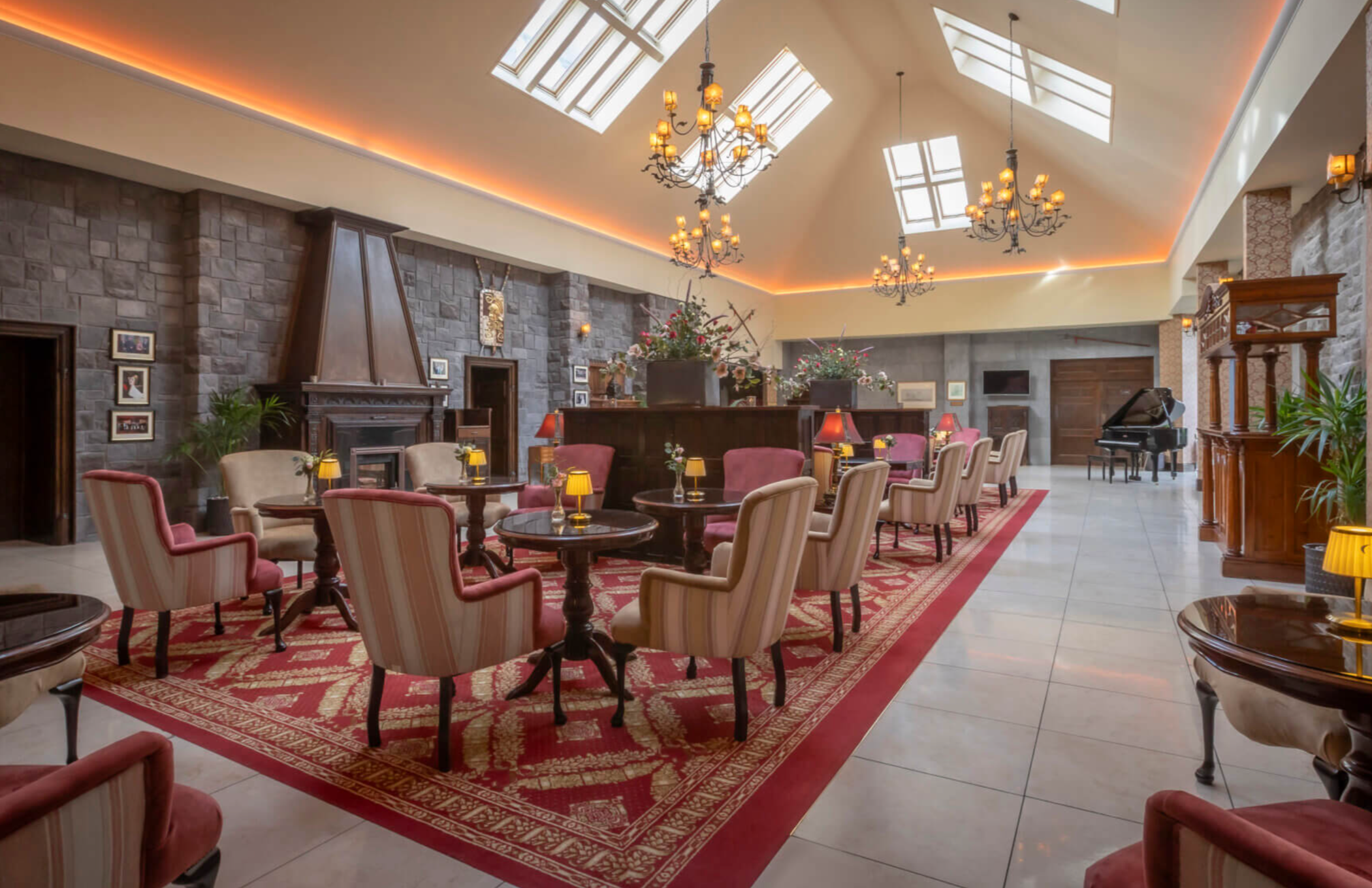 Bright lobby featuring ornate dining tables and chairs under chandeliers and next to a grand piano.