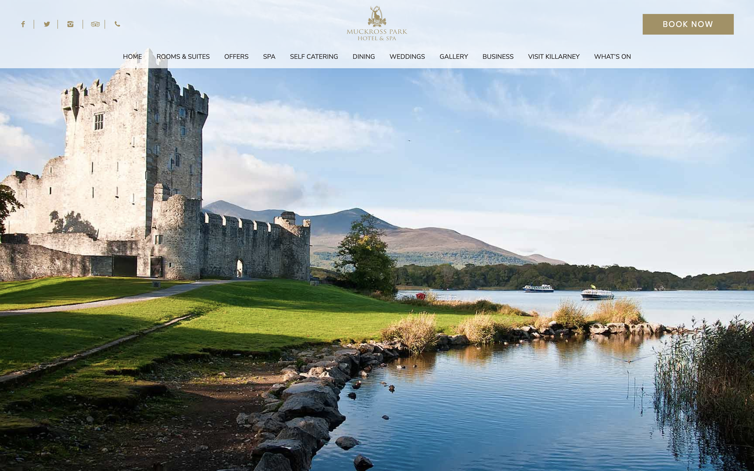 Scenic outdoor shot of a castle ruin, on the shore of a lake, with mountains in the distance.