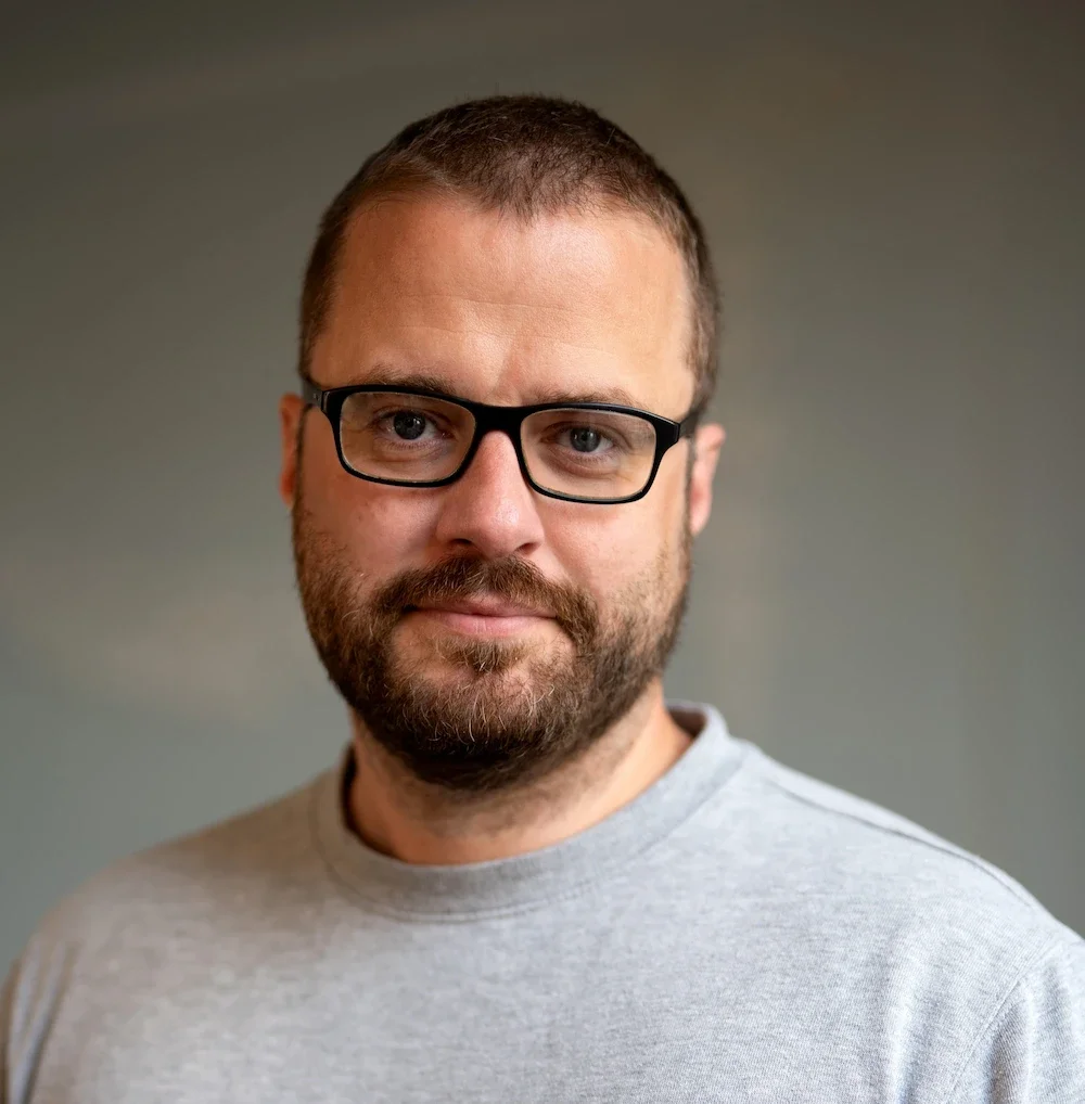 Portrait of The Copy Concierge and his glasses, beard, short brown hair and smile.