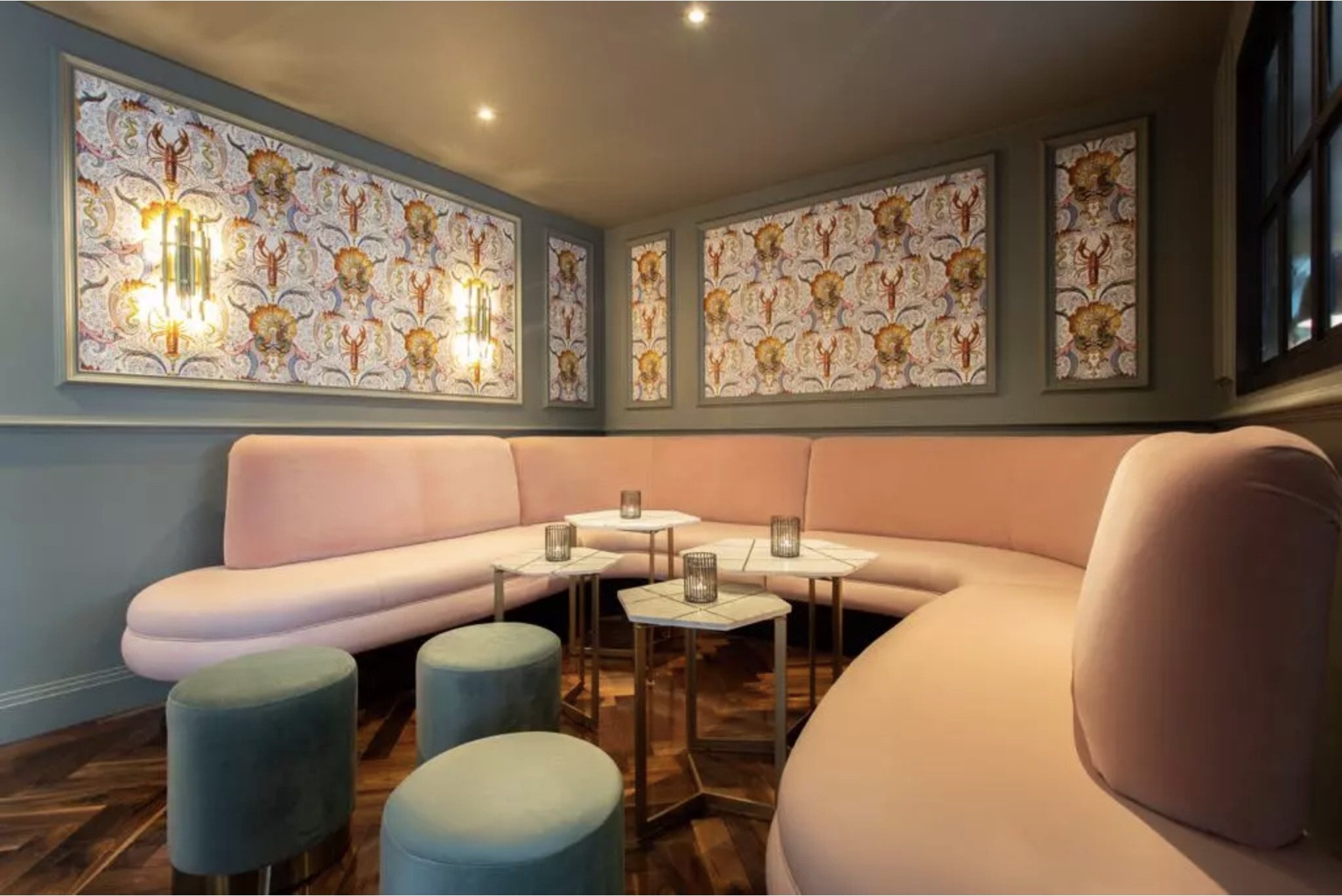 Stylish corner of the bar with a long pink wraparound bench and four small tables with candles.