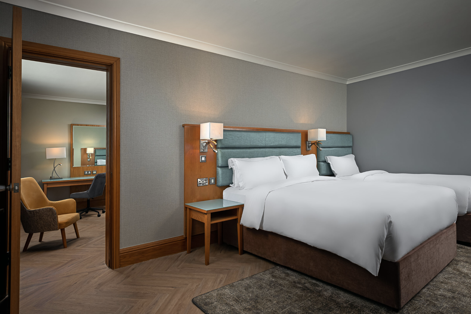 Spacious twin room with a double bed, single bed and two large, blue, padded headboards above each.