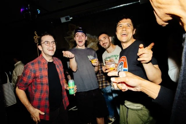 Group of four men smiling and holding drinks at a social gathering or party.