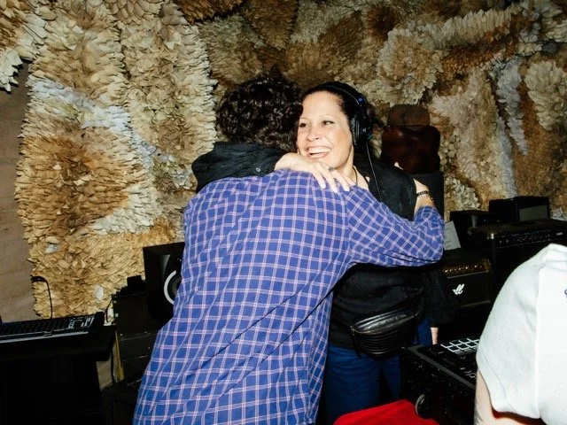 A woman smiling and hugging a man in a recording studio with soundproofing foam on the walls.