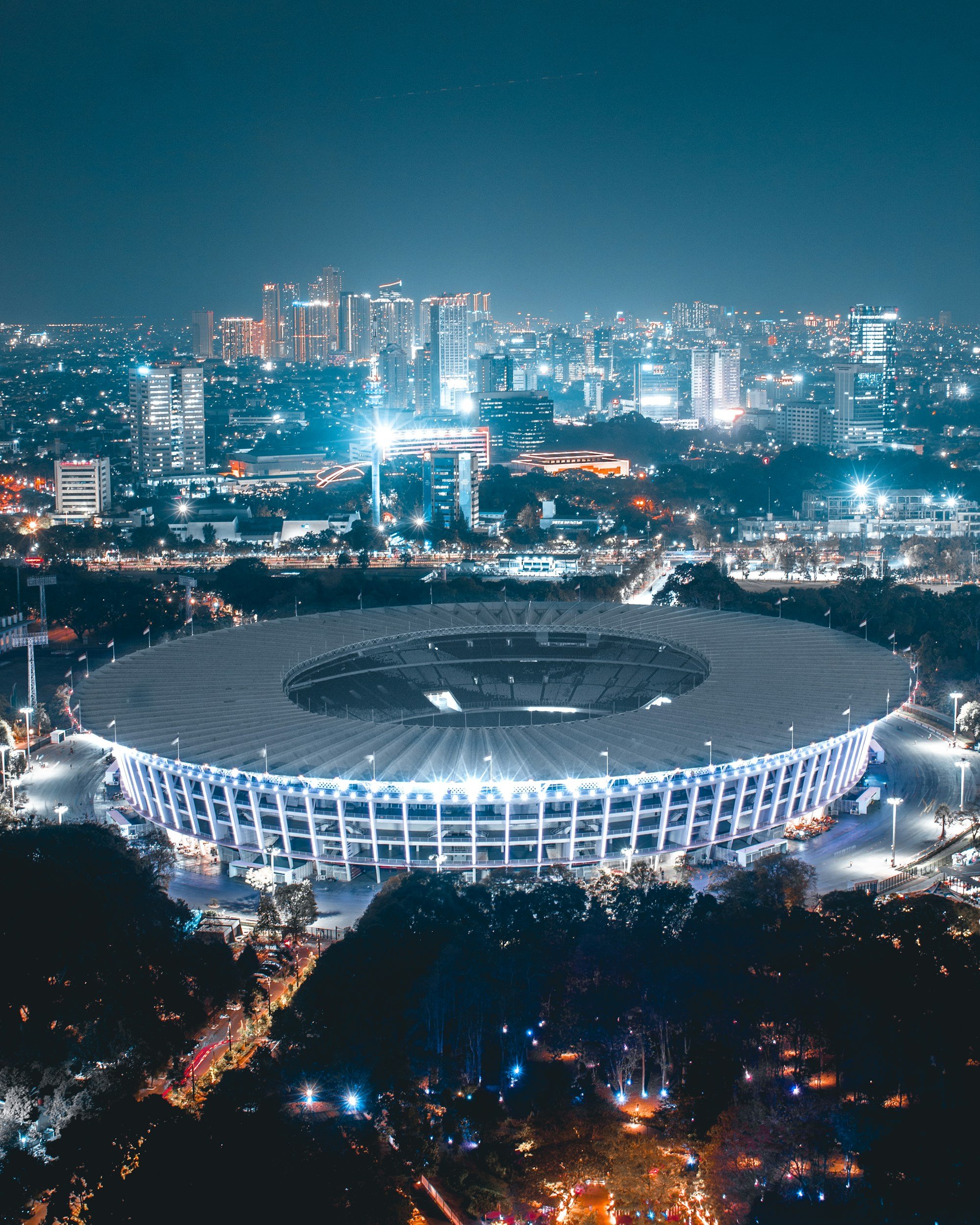 Night view of a large, illuminated stadium surrounded by city buildings and streets in an urban area.