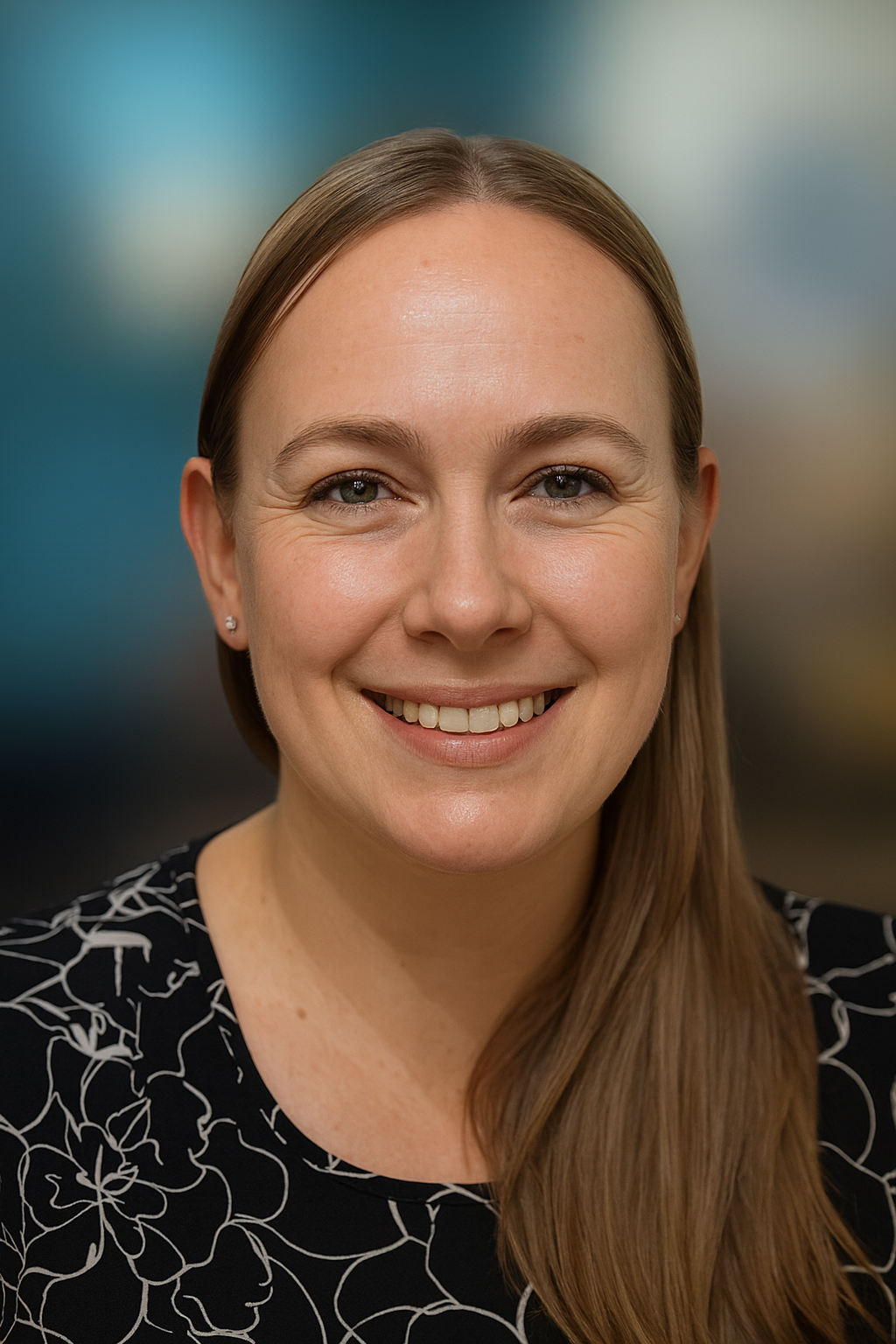 Close-up of a woman with long straight hair smiling at the camera, wearing a black top with white floral pattern, small earrings, and a plain background.