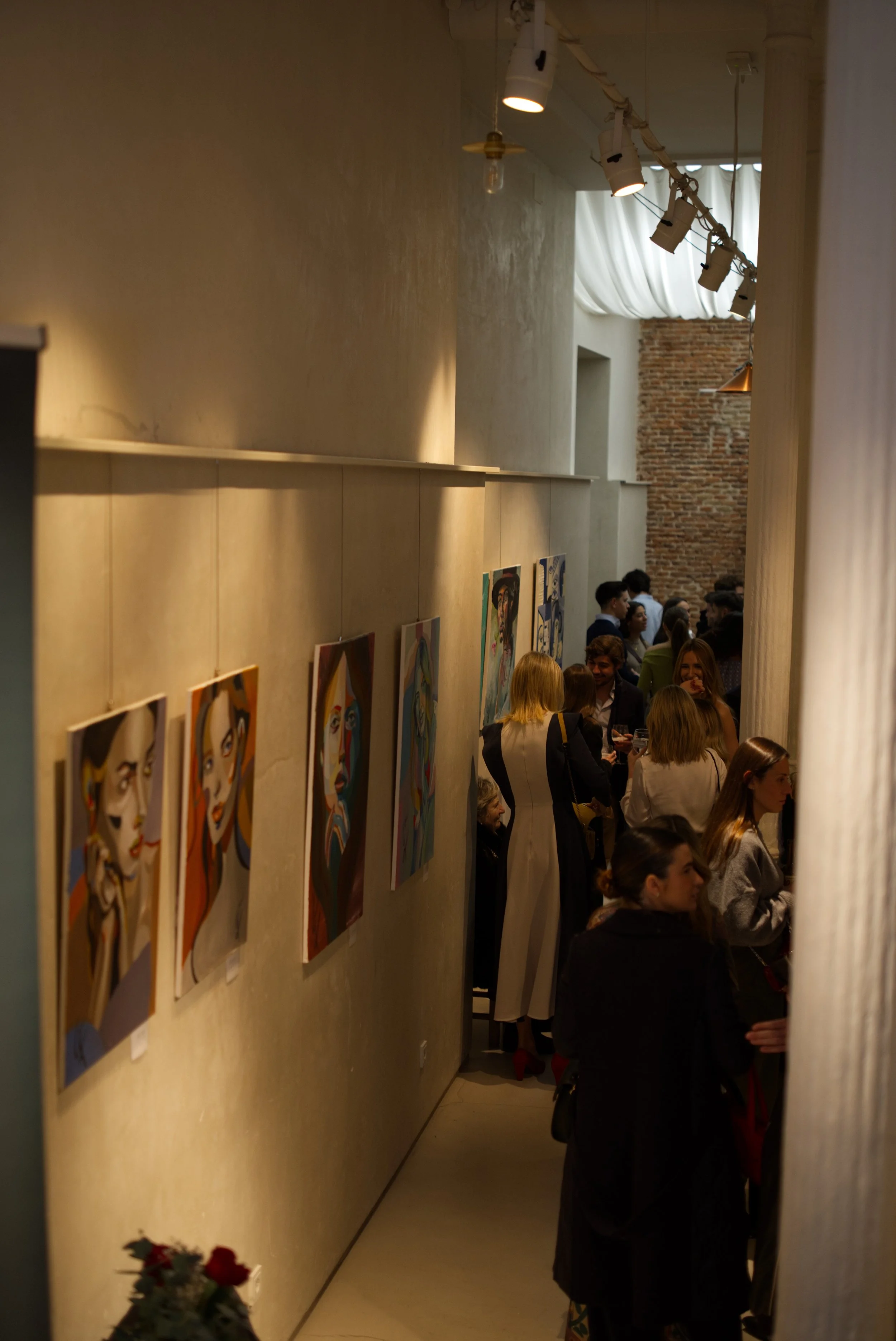 Una galería de arte con pinturas en la pared y varias personas observando las obras en un evento cultural.