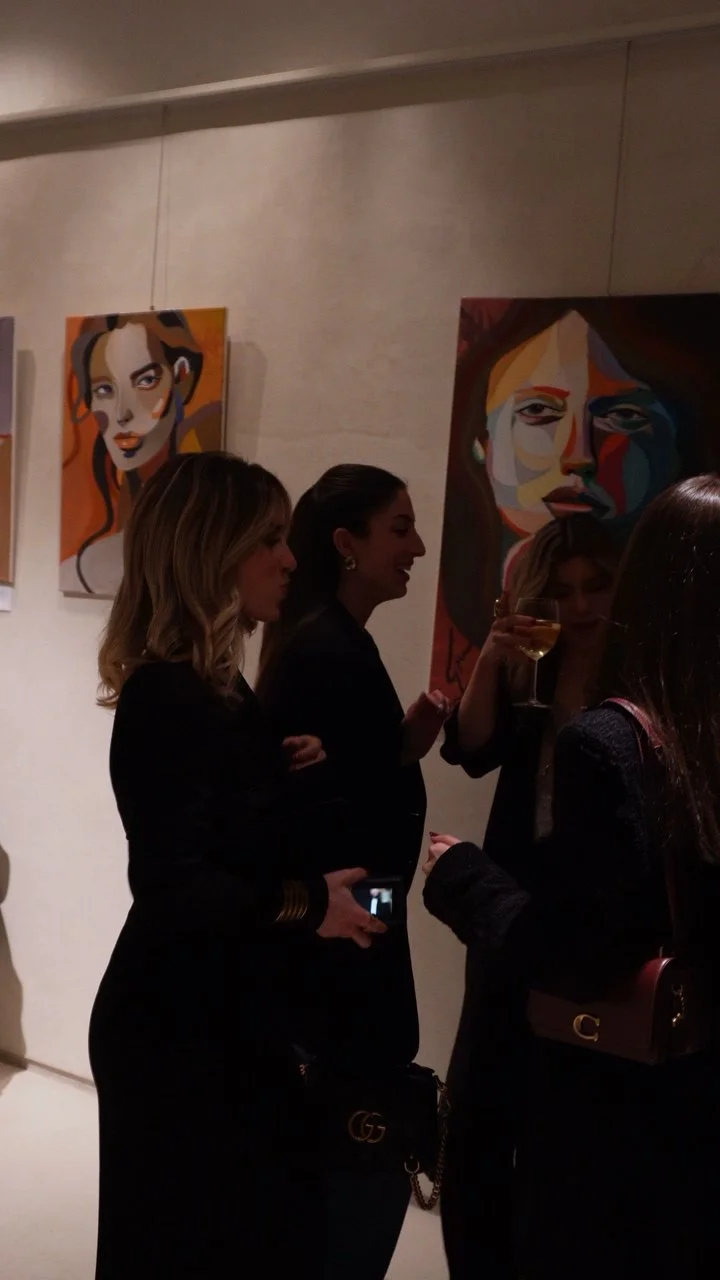 Grupo de mujeres en una galería de arte, conversando y disfrutando. Pinturas abstractas de retratos femeninos en la pared.
