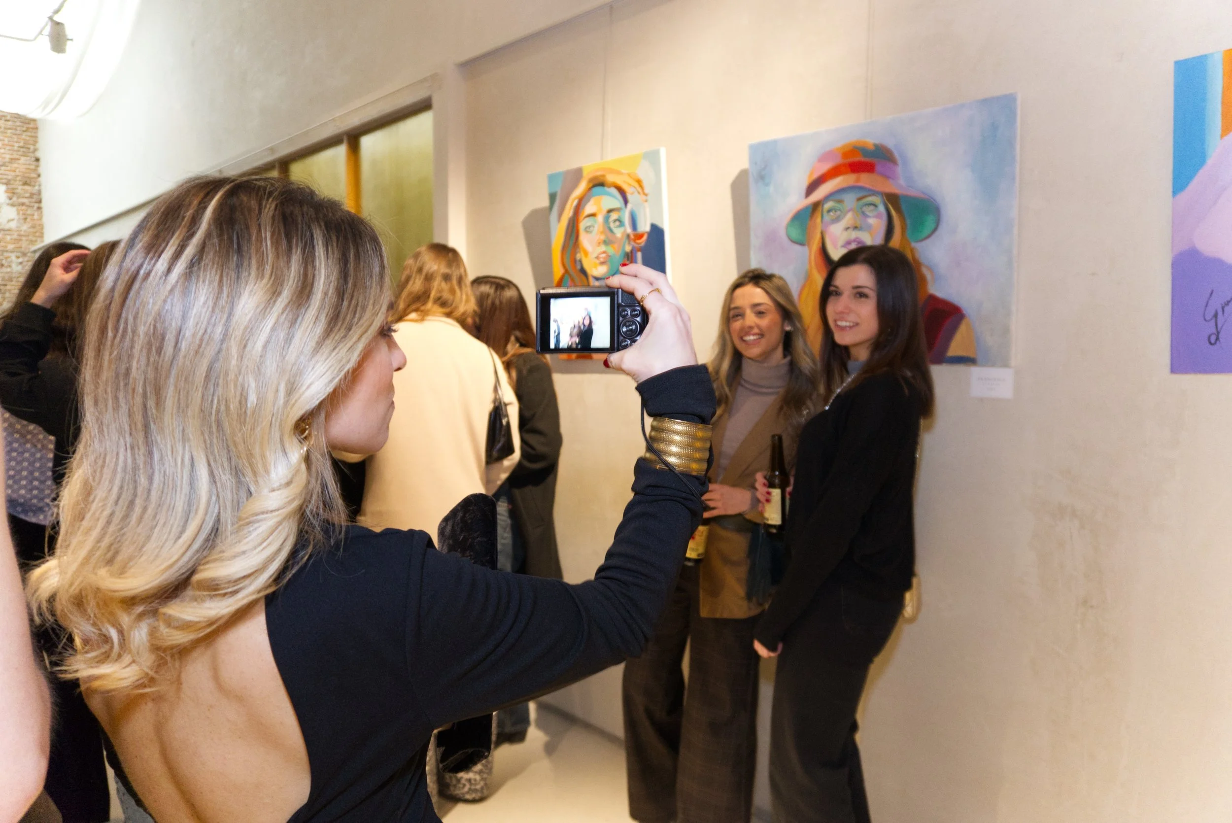 Mujer tomando una foto de dos mujeres en una galería de arte, con pinturas coloridas en la pared.