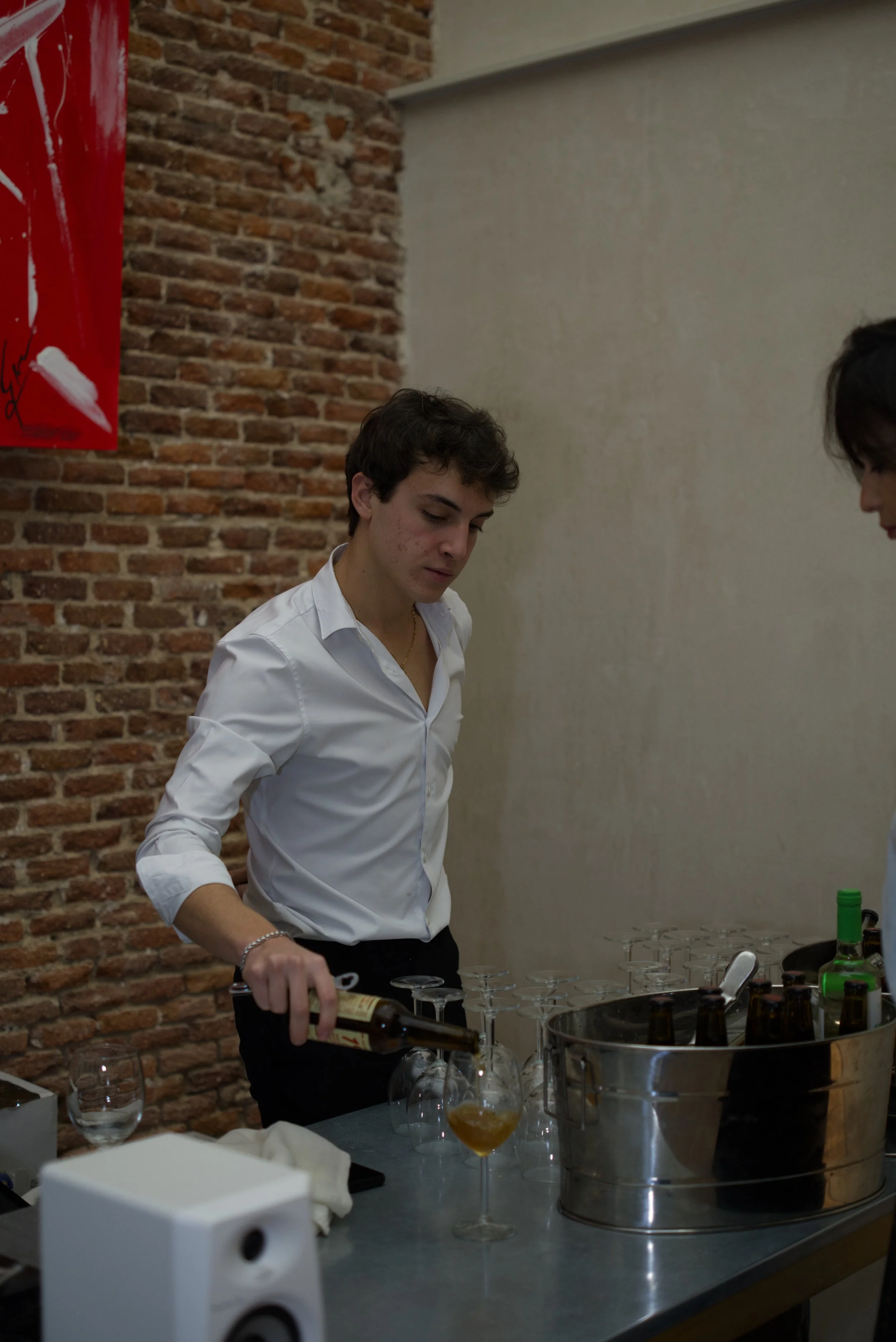 Joven sirviendo bebida en copa de cóctel en bar o reunión social con fondo de pared de ladrillos.