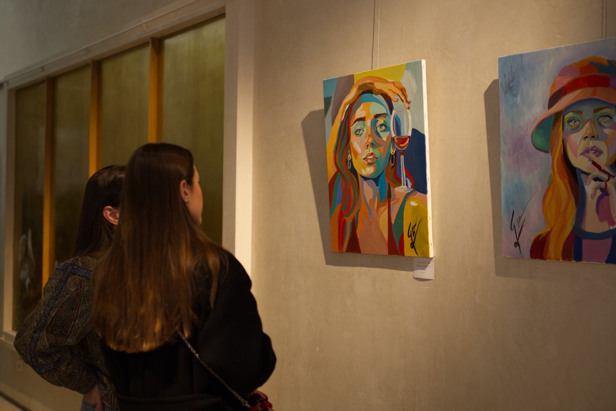 Dos mujeres observando pinturas coloridas en una galería de arte.