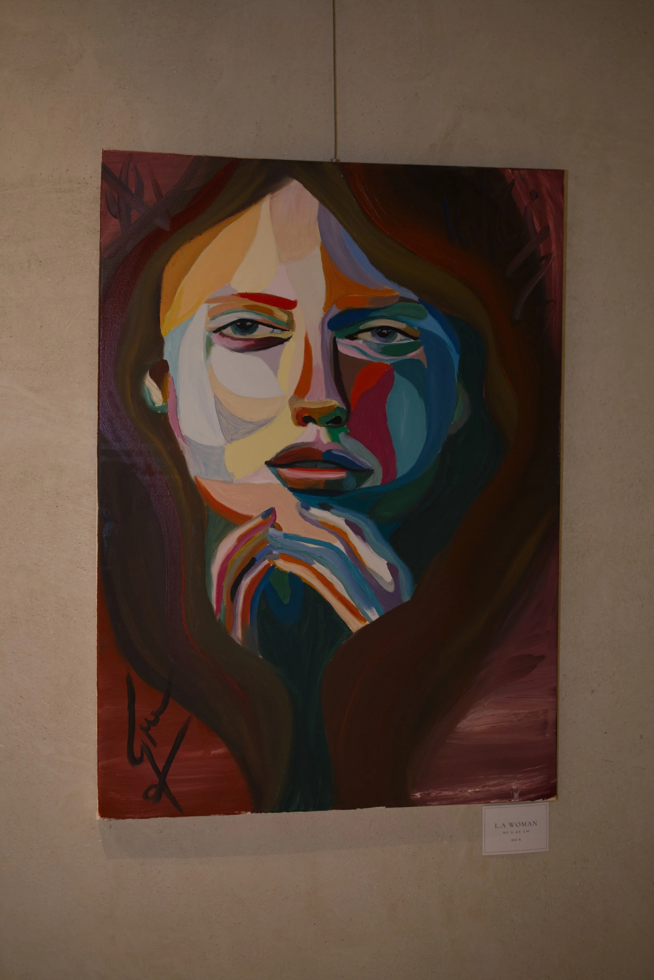 Retrato artístico de una mujer con cabello largo y oscuro, con expresión seria. La obra es en estilo abstracto, con formas y colores vibrantes, con tonos cálidos y fríos.