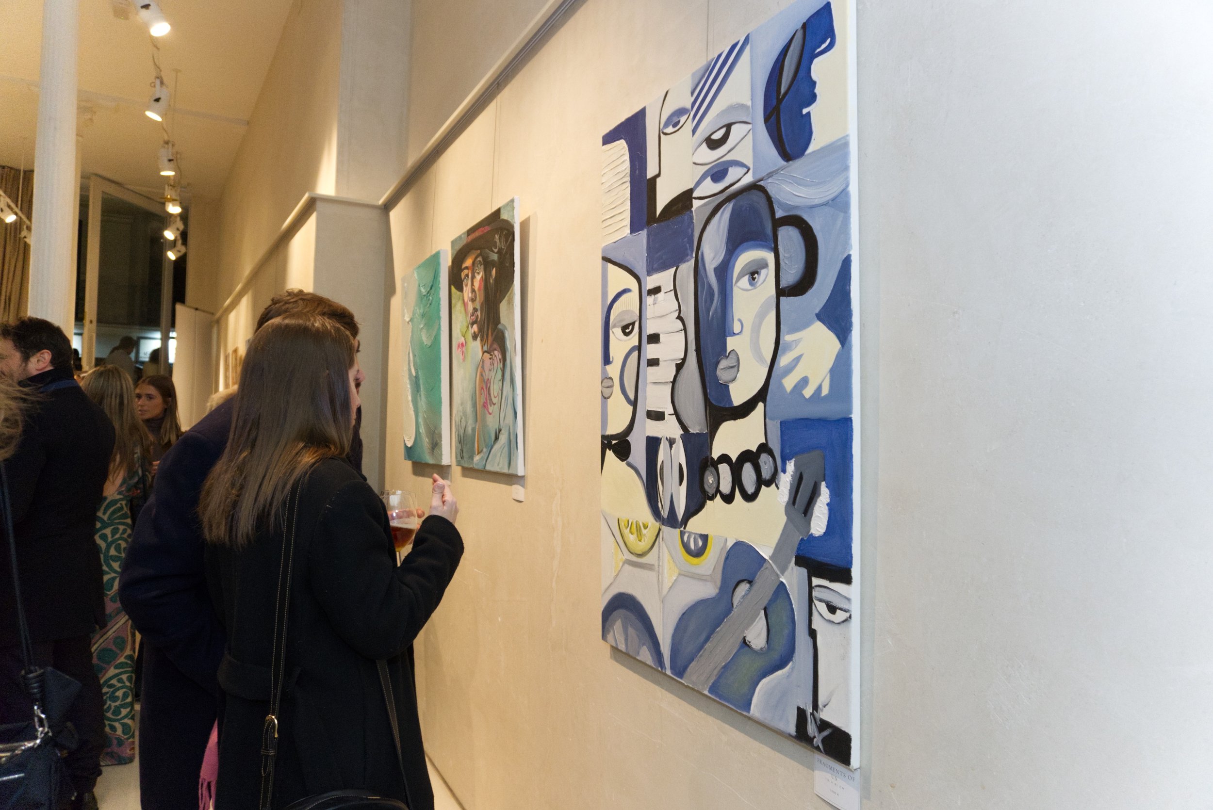 Personas observando pinturas en una galería de arte con paredes blancas y iluminación dirigida