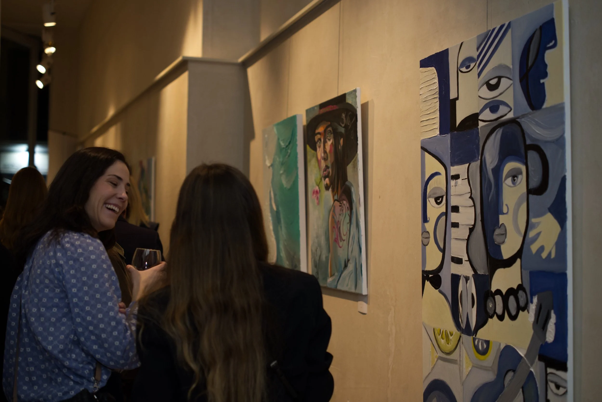 Mujeres disfrutando y conversando en una galería de arte con obras abstractas en las paredes.