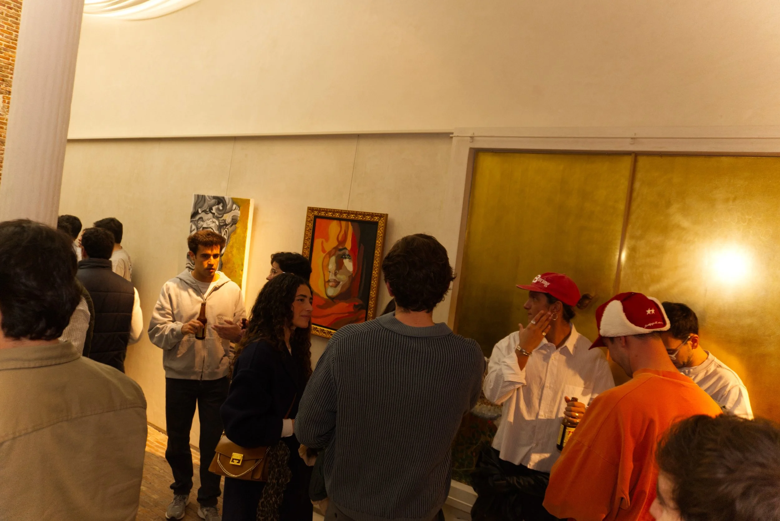 Varias personas conversando en una galería de arte con pinturas en las paredes.