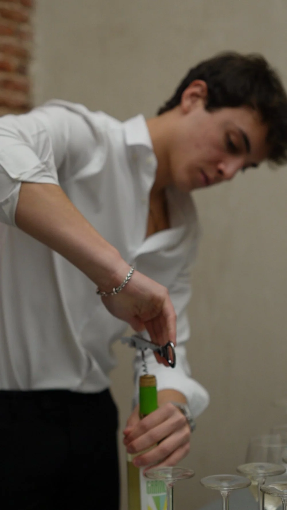 Joven sirviendo vino de una botella en copas de cristal.
