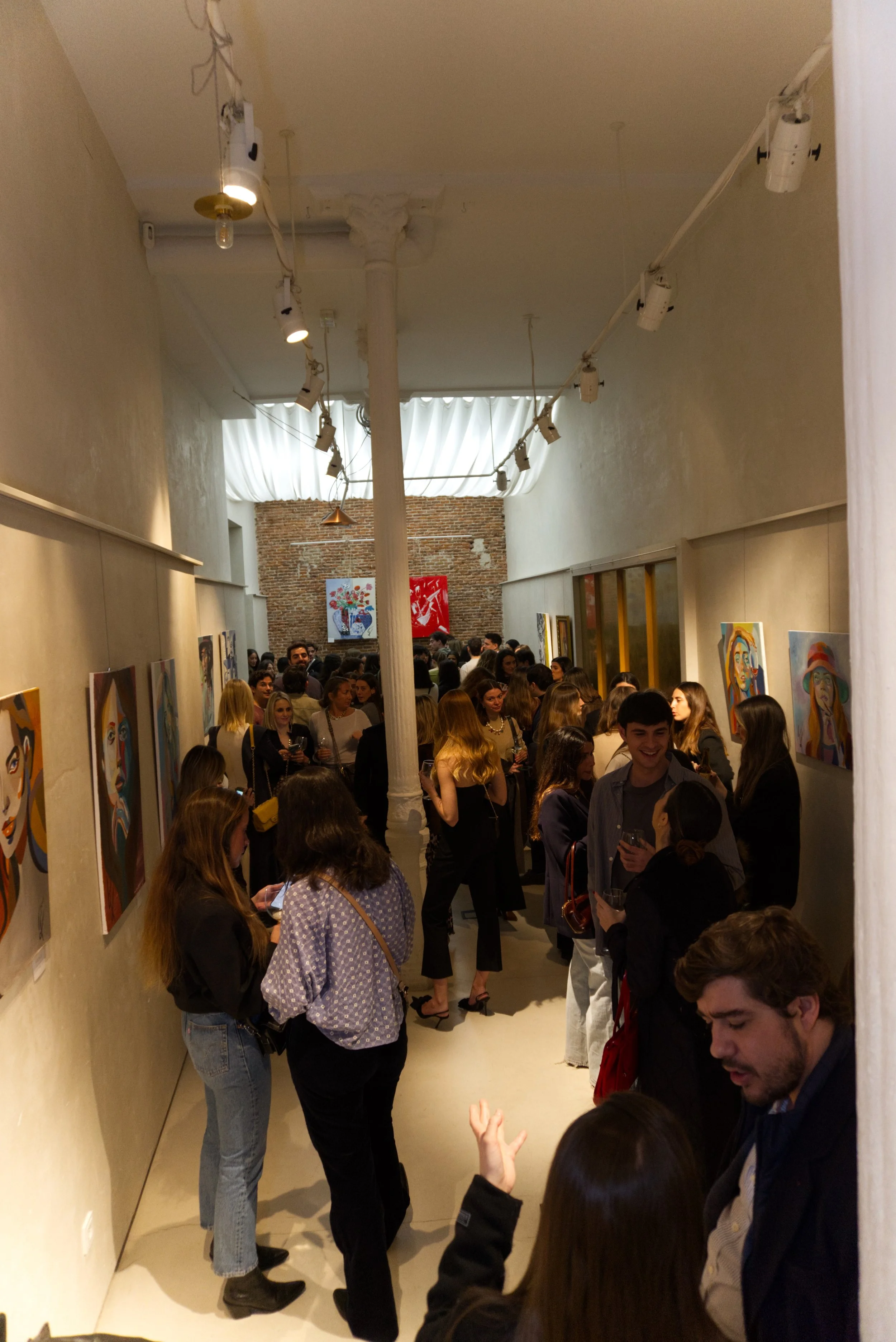 Galería de arte con muchas personas observando pinturas en las paredes en un evento cultural.