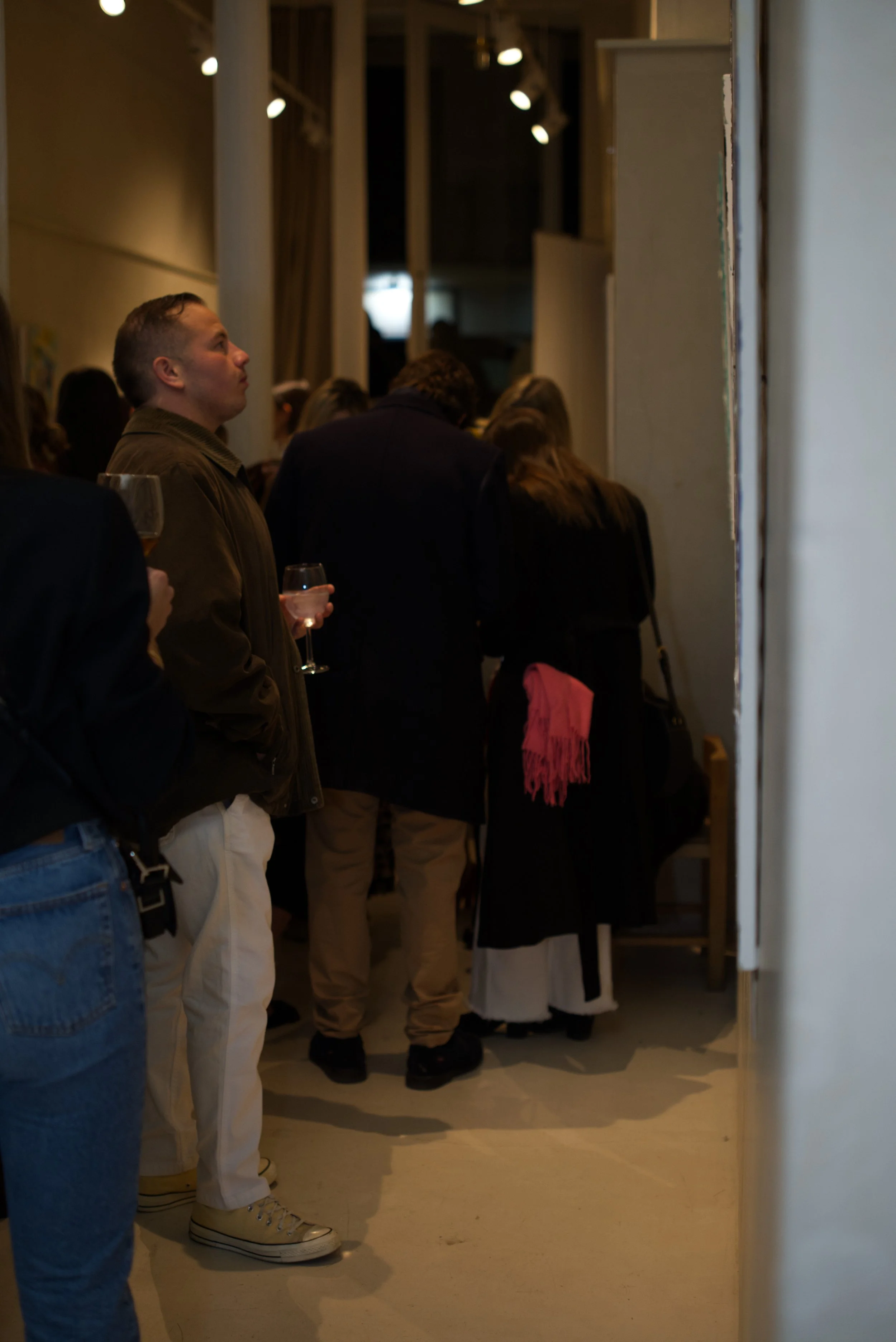 Personas en un evento social, algunas sosteniendo copas de vino, en un espacio interior con iluminación tenue.