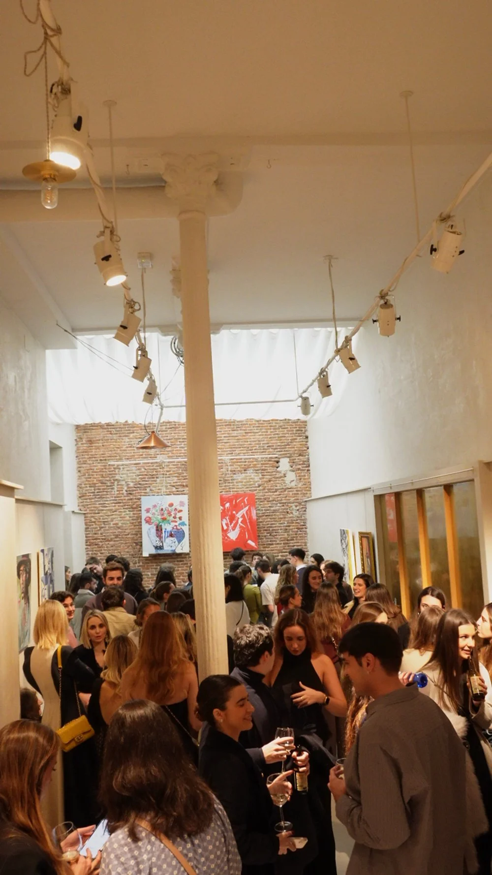 Gente en una galería de arte, observando y conversando, con paredes decoradas con cuadros, en un espacio bien iluminado y con un estilo moderno y clásico.