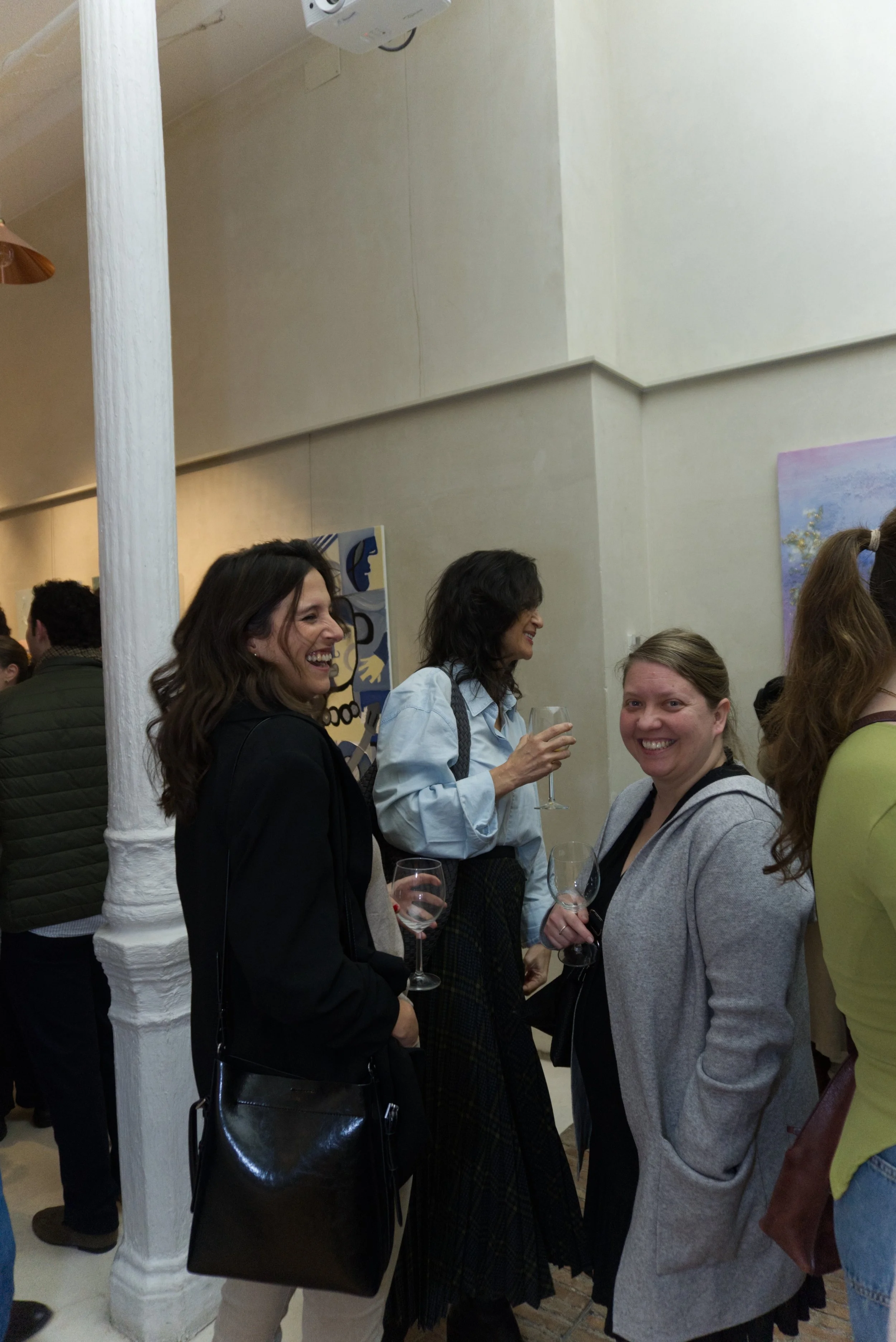 Grupo de personas sonriendo y conversando en una galería de arte, algunas sosteniendo copas de vino.