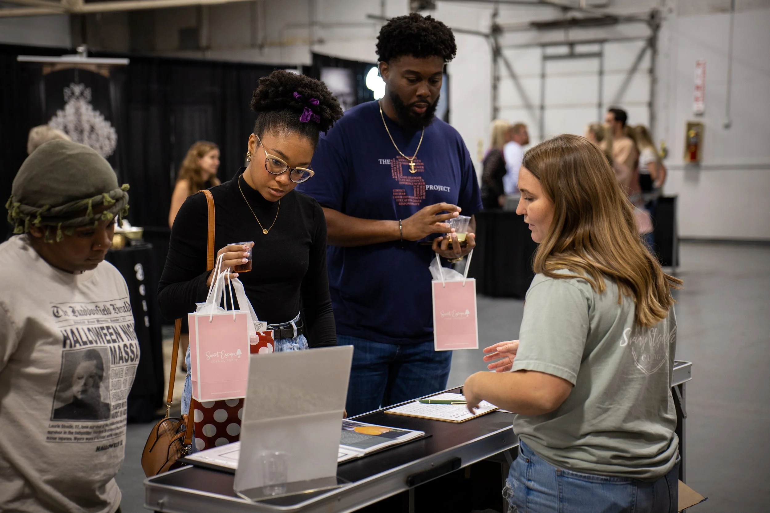 Group of four people purchasing at a table with a woman assisting them at an indoor event.