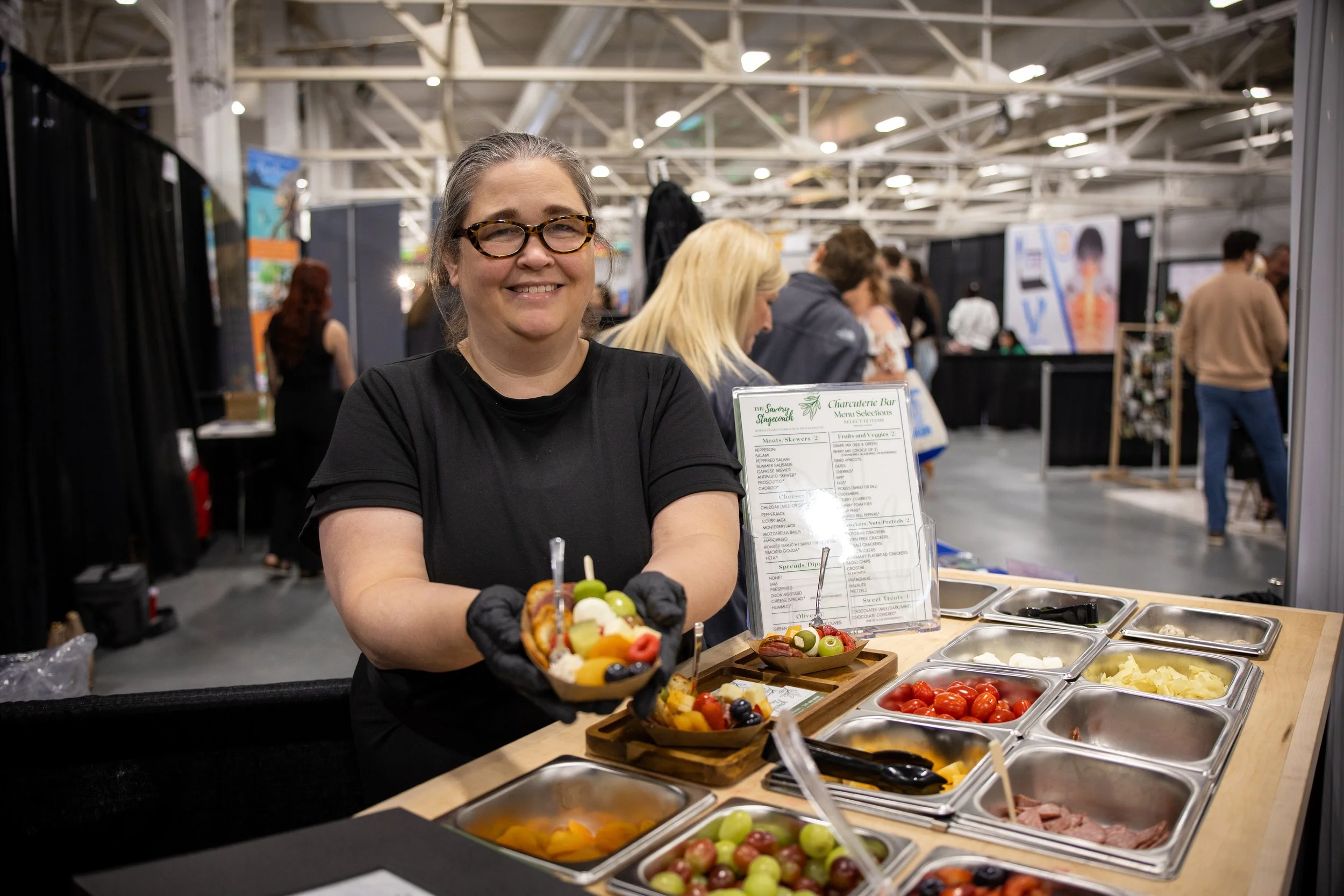 Woman serving fruit and yogurt parfait at a food stall in an indoor event.