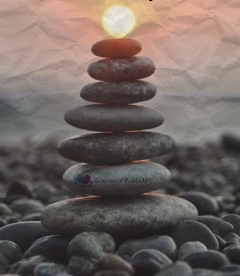 Balanced stack of smooth stones topped with a glowing white stone on a rocky beach, symbolizing mindfulness and positivity