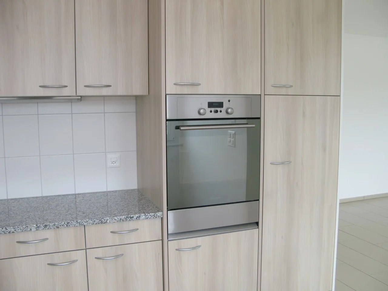 Küche mit Holzschränken, grauer Granit-Arbeitsplatte und eingebautem Edelstahlofen