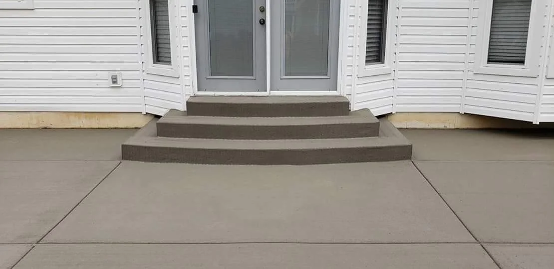 Concrete steps leading up to a glass door with two sliding panels, outside a house with white siding and a concrete porch.