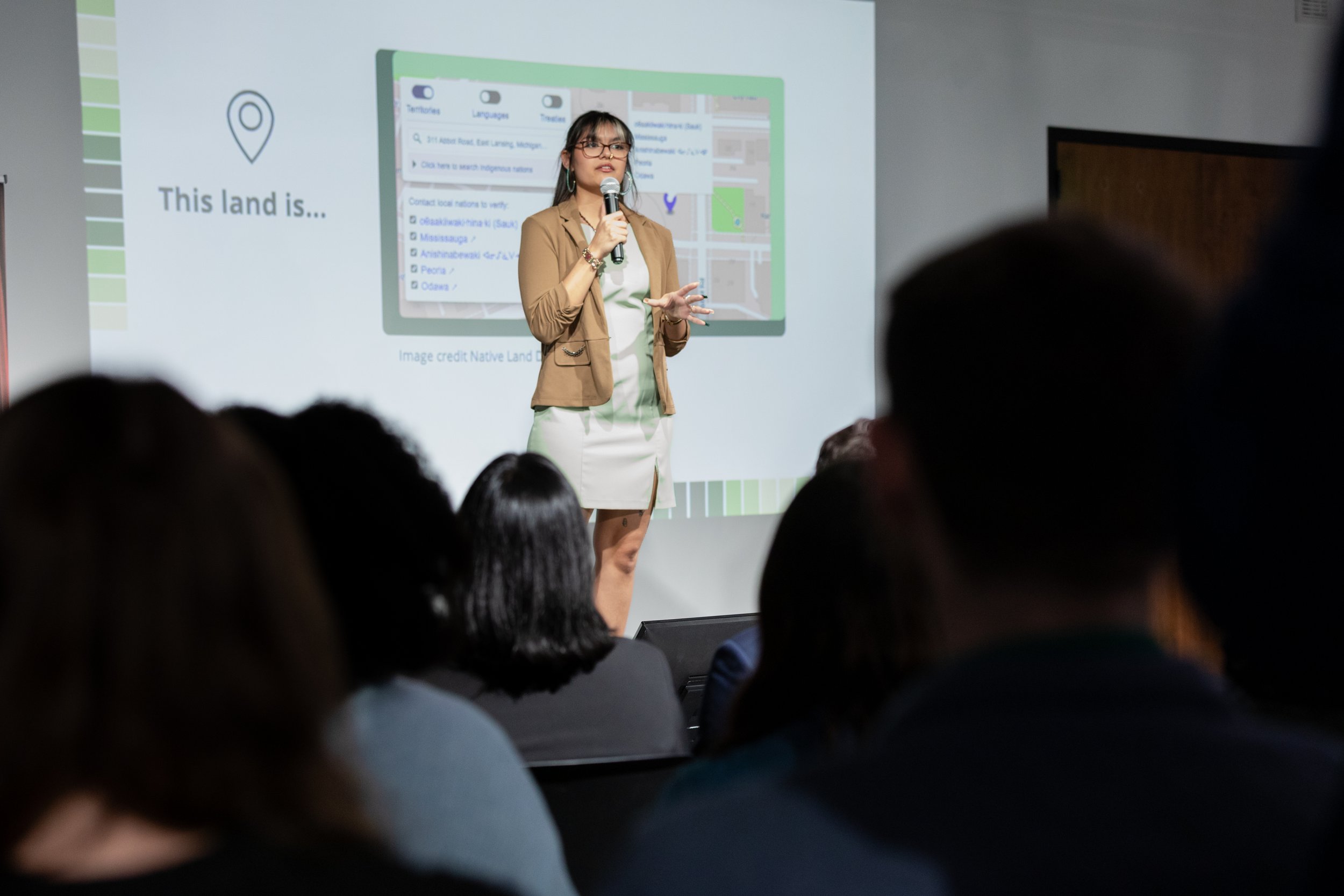 Nevaeh Ramon standing on a stage in front of a projected screen, holding a microphone.