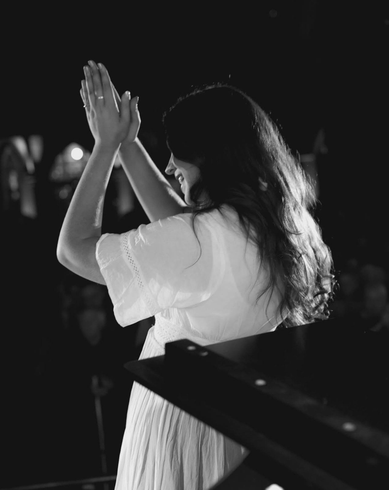 A black and white image showing Niamh facing away from the camera, clapping at an audience during one of her live sets. She is wearing a white dress.