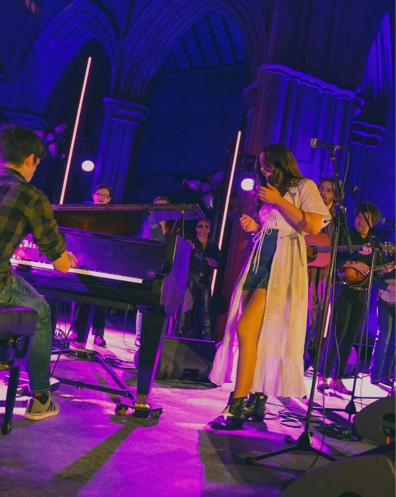 Niamh performing on stage with her pianist. She is wearing a long white dress boots, and the stage is lit in purple.