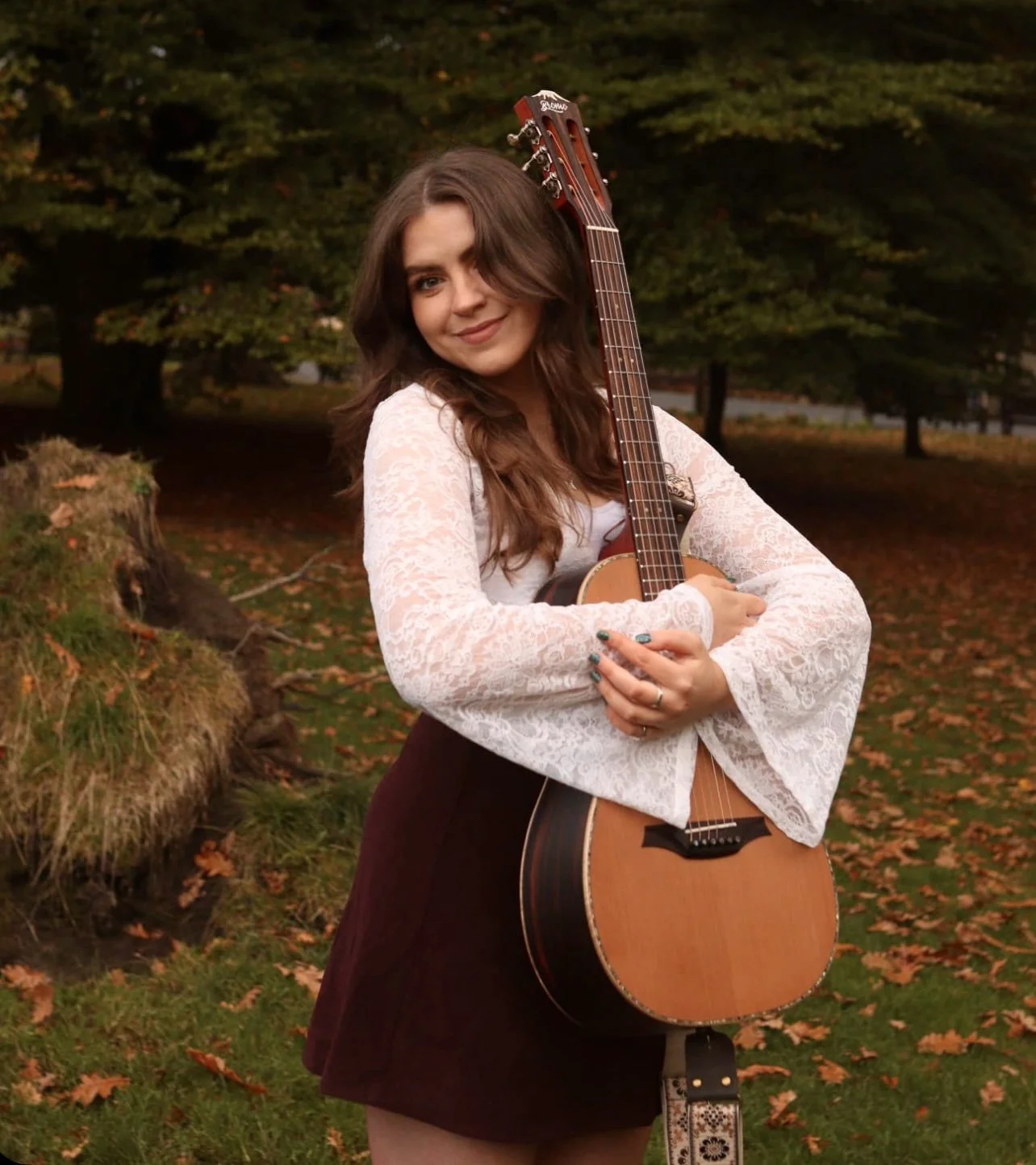 Niamh holding an acoustic guitar, wearing a light blouse and a dark skirt.