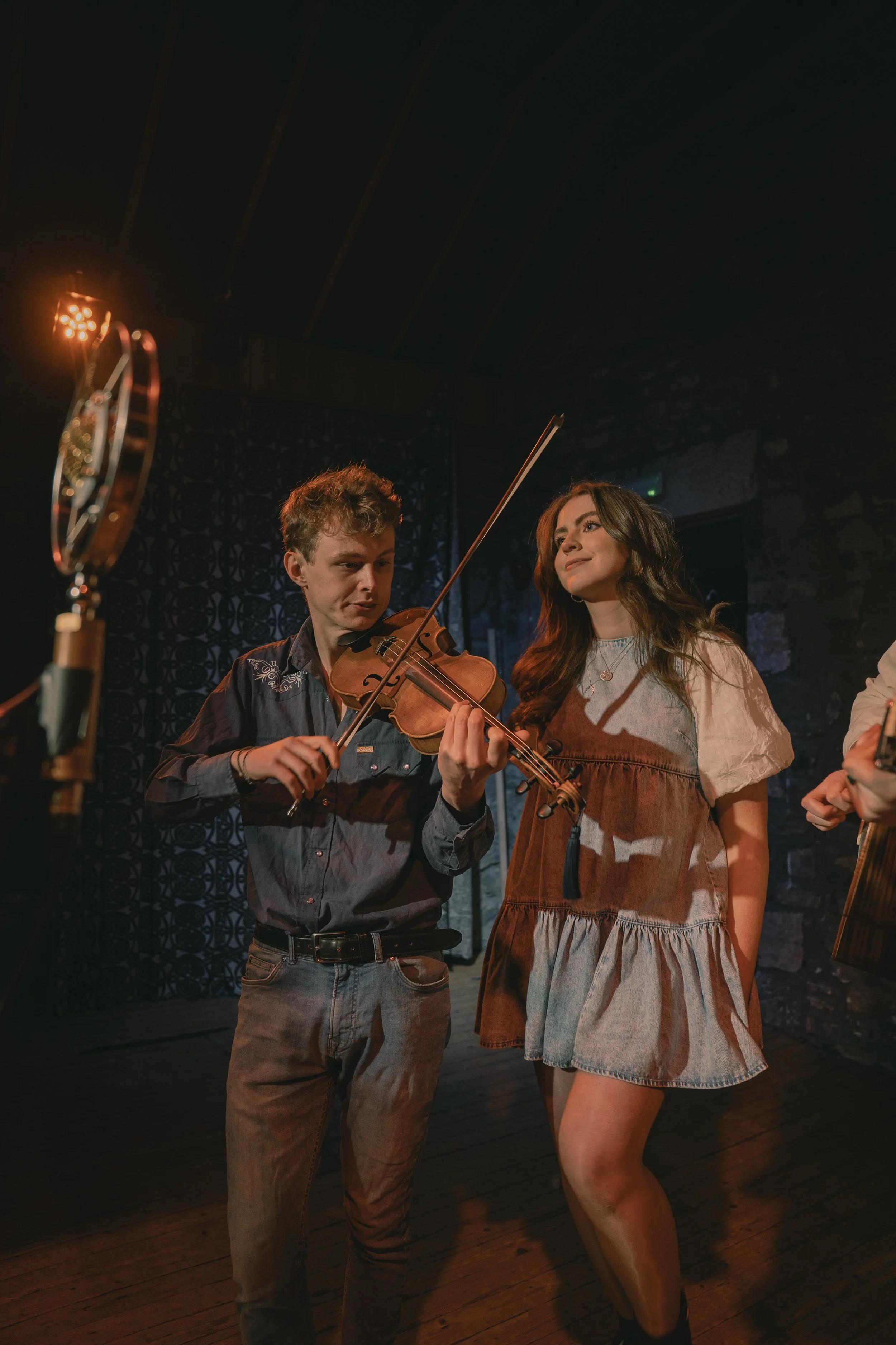 Niamh singing on stage alongside her fiddle player in a dimly lit music venue.