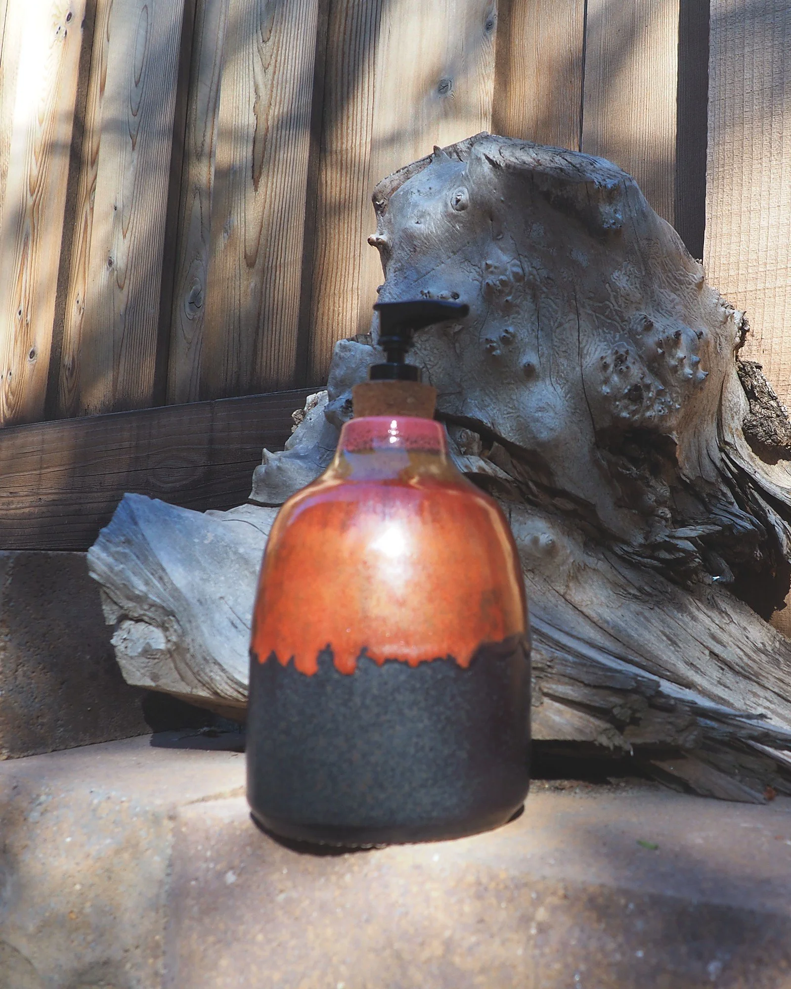 Ceramic soap dispenser beside driftwood against a wooden fence